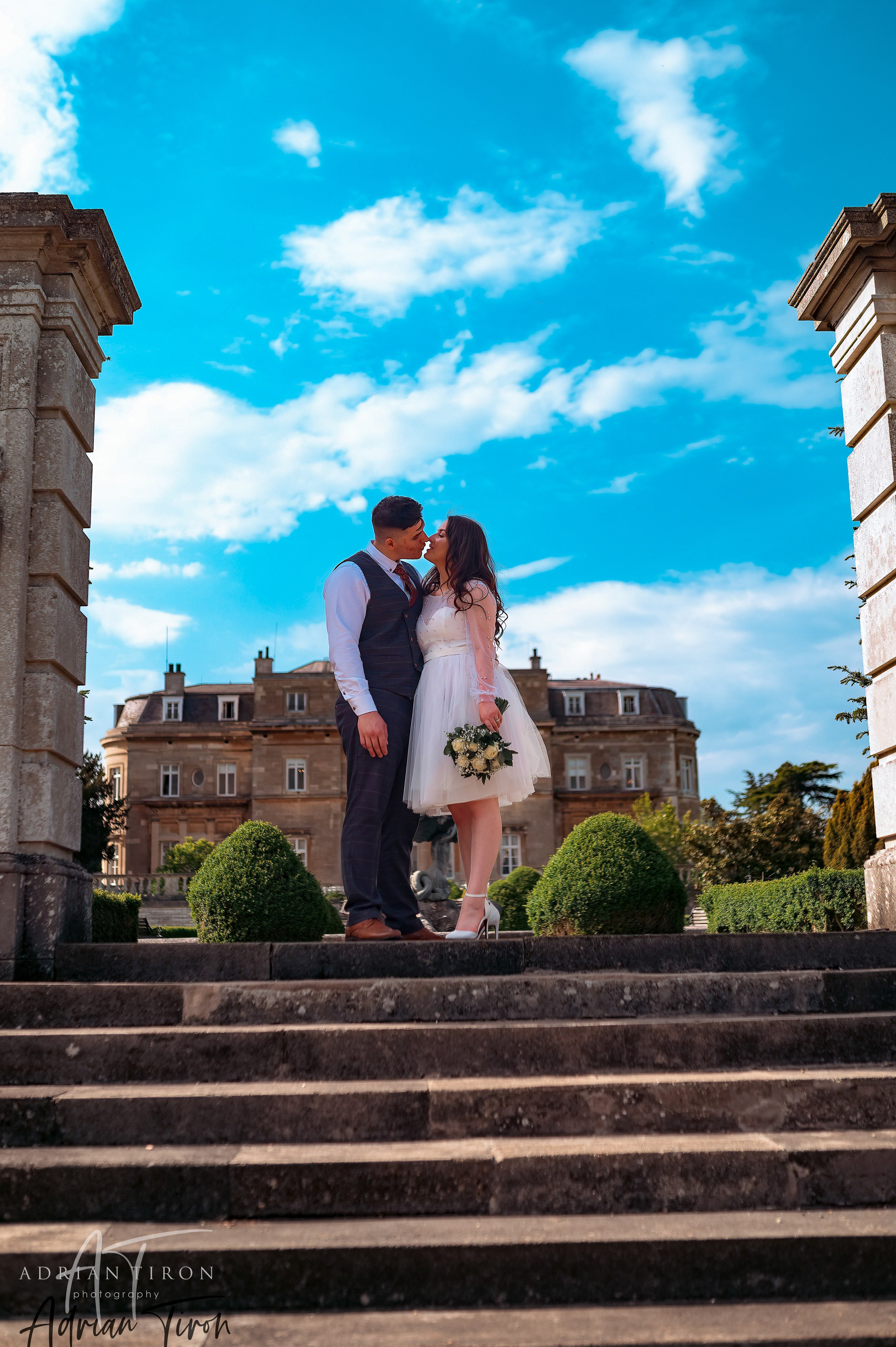 Bride and groom kissing on stone steps at Luton Hoo under a clear blue sky