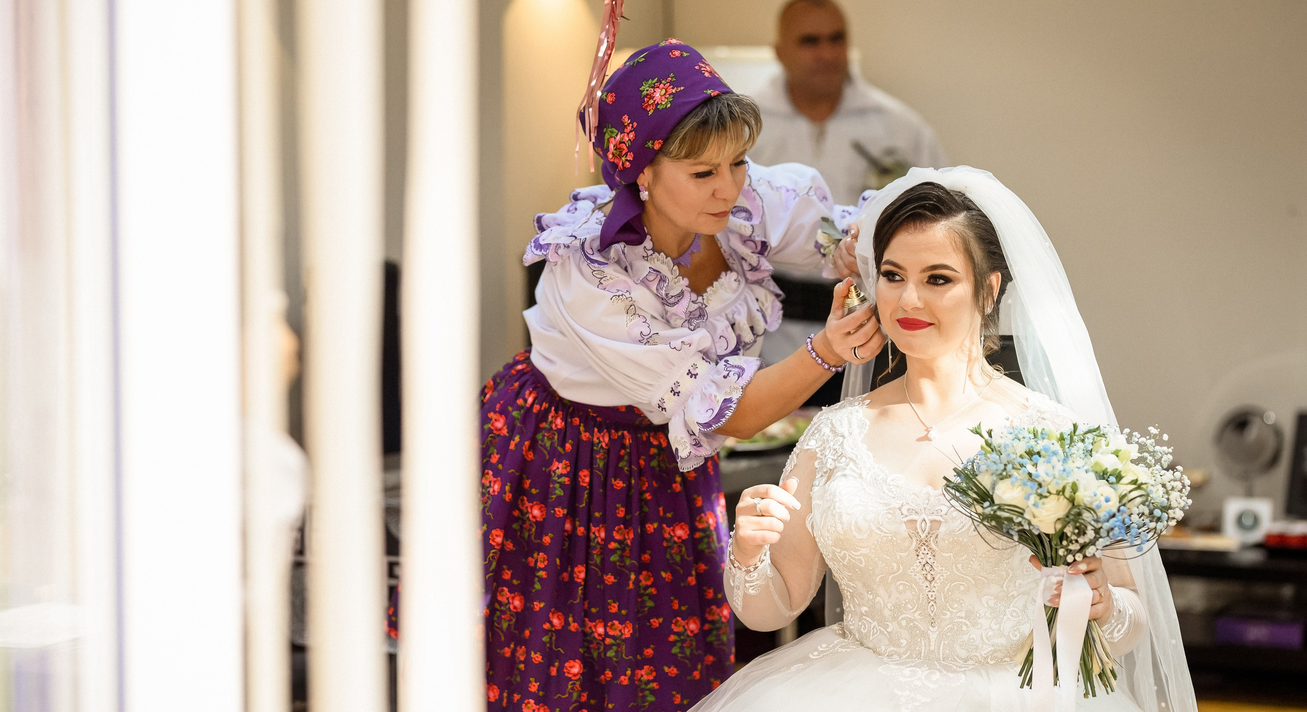 An older relative adjusting the bride’s veil, wearing a colourful traditional headscarf