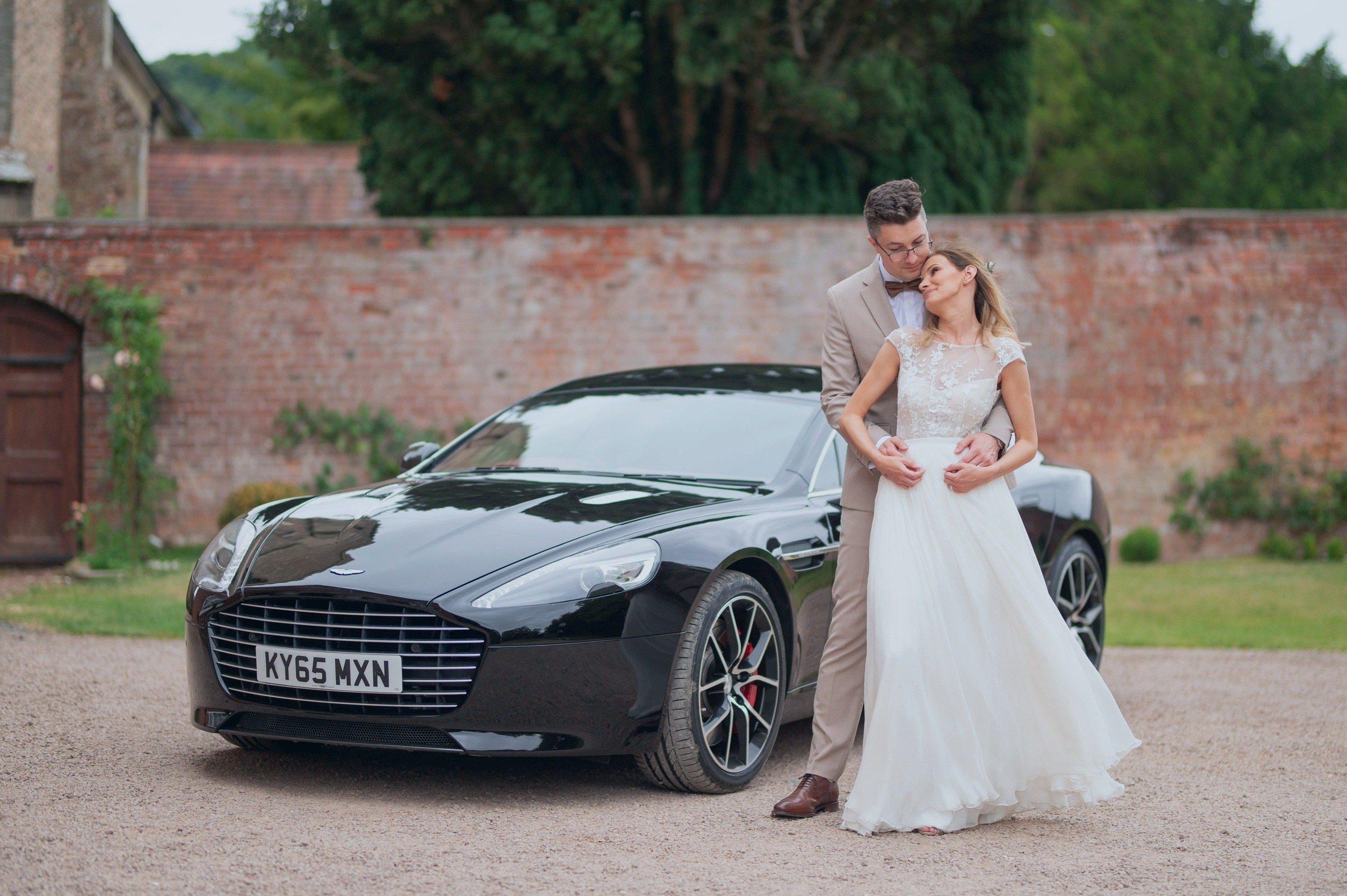 Bride and groom embracing beside their black Aston Martin wedding car, Charlecote Pheasant Hotel