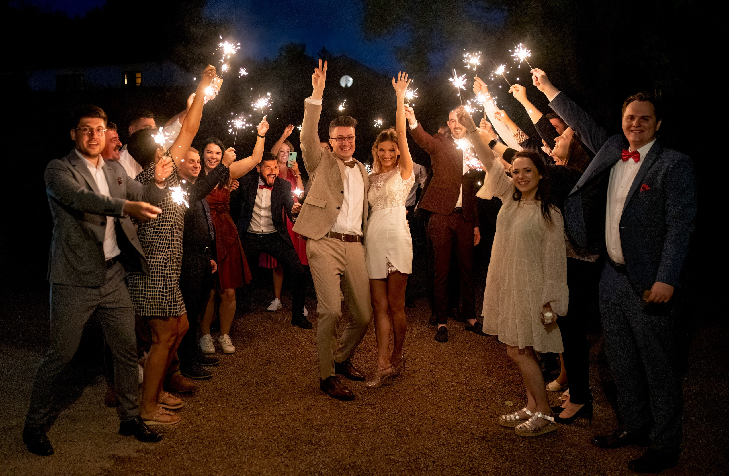 Bride and groom celebrating with arms raised in the sparkler send-off, guests cheering around them