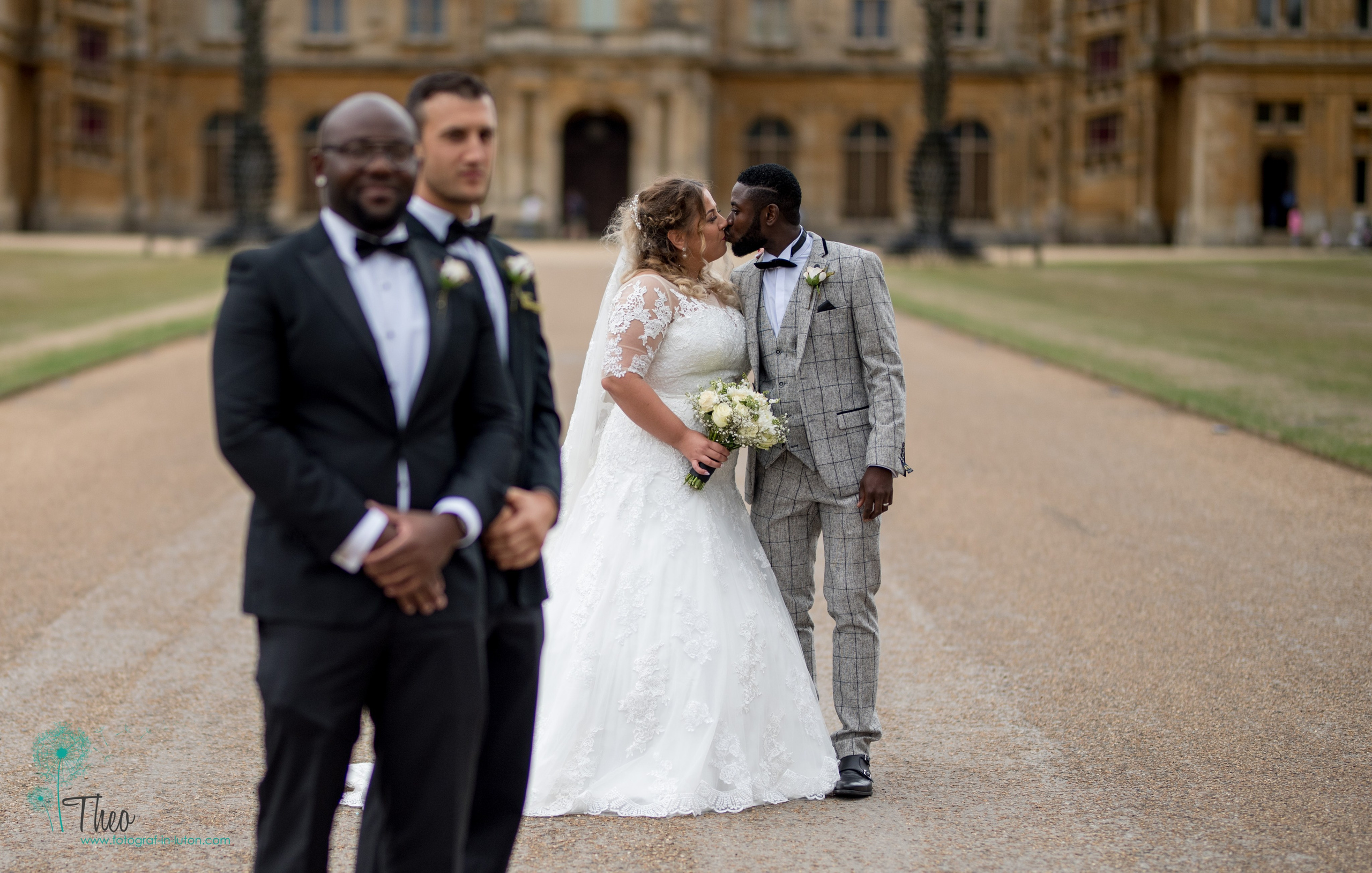 A tighter crop of the groomsmen smiling as the newlyweds kiss in the blurred background at Waddesdon Manor