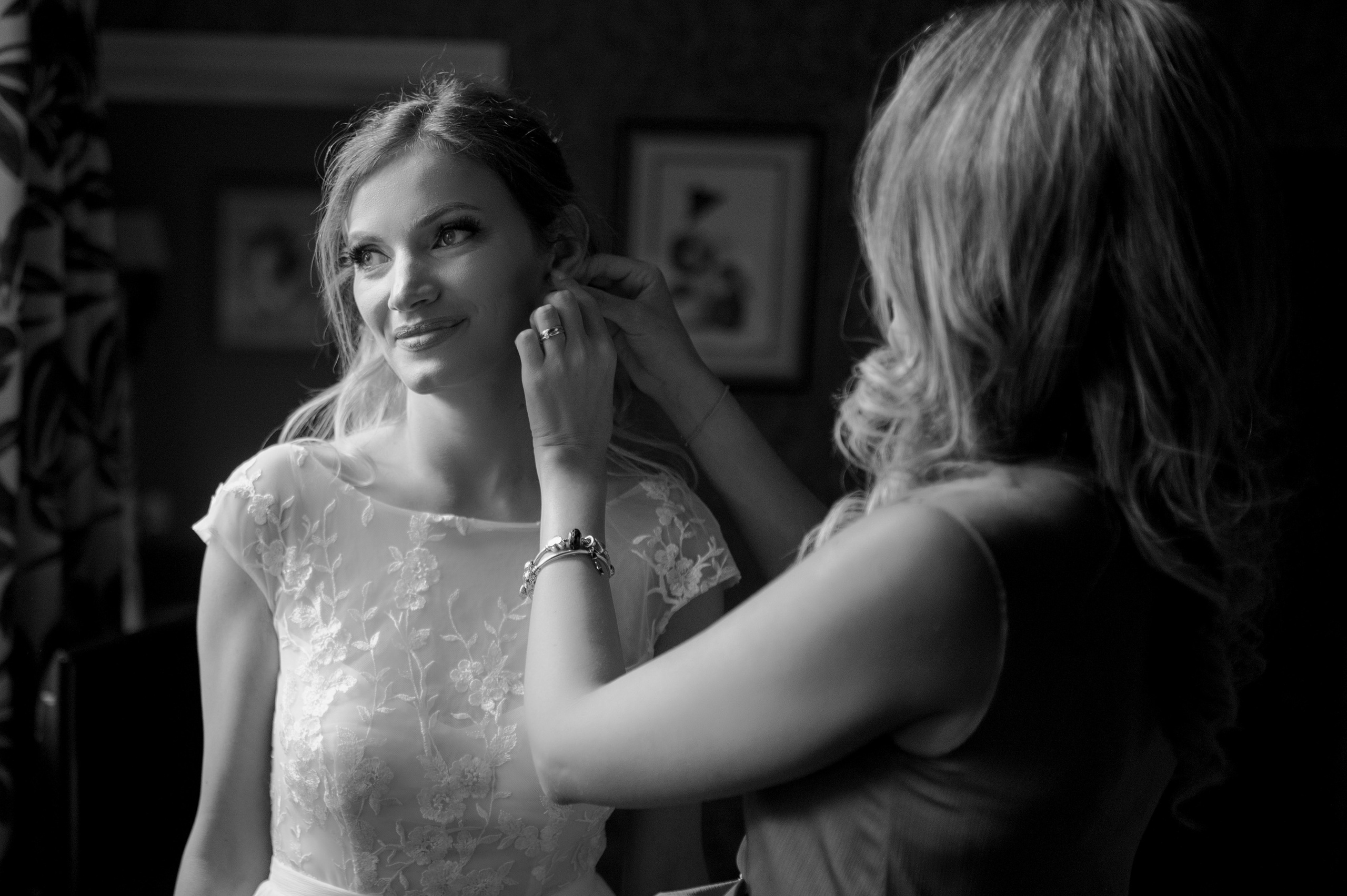 Bridesmaid fastening the bride's earring, both smiling (black and white)