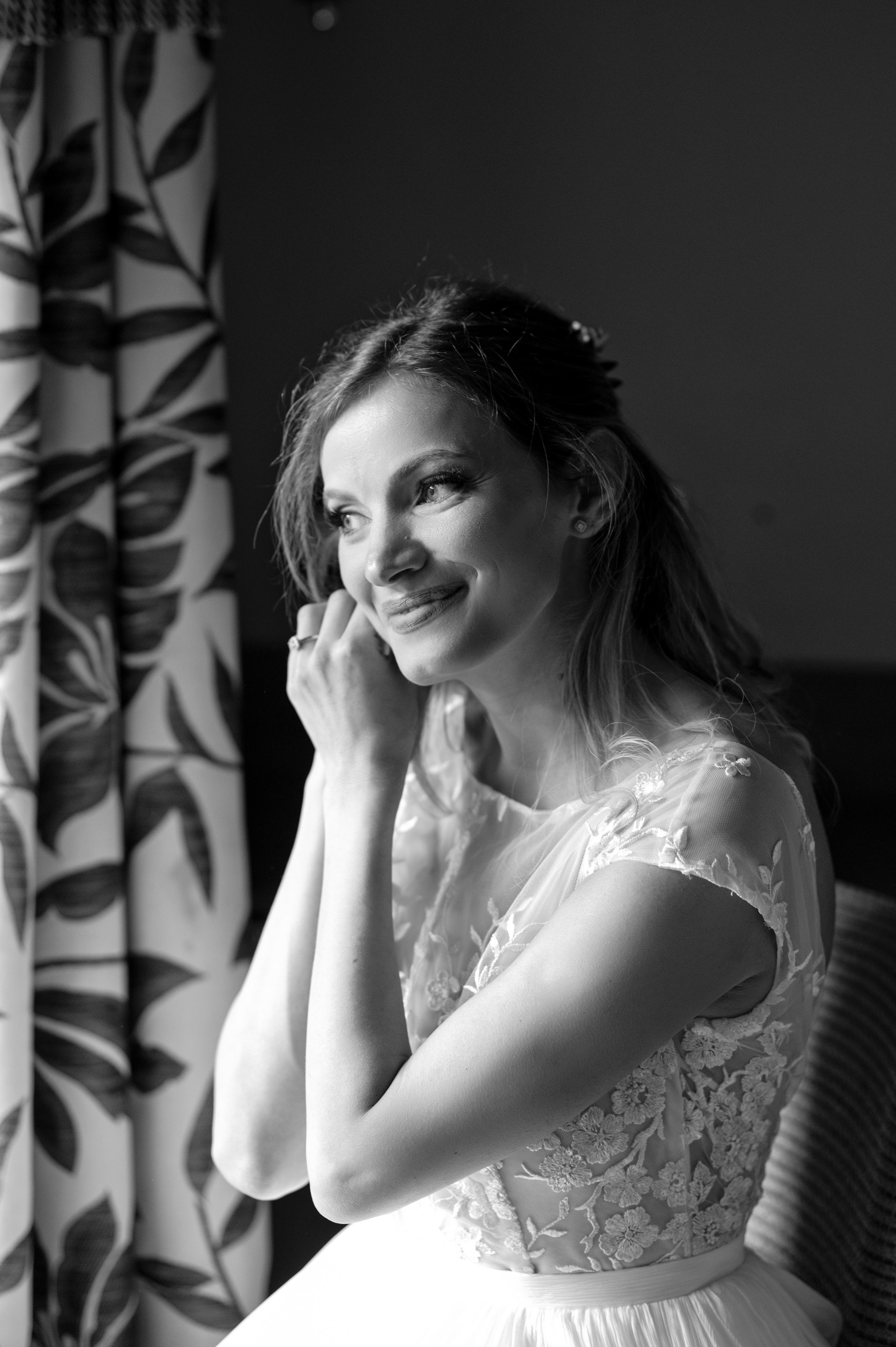 Bride smiling by the window during bridal prep, natural light (black and white)