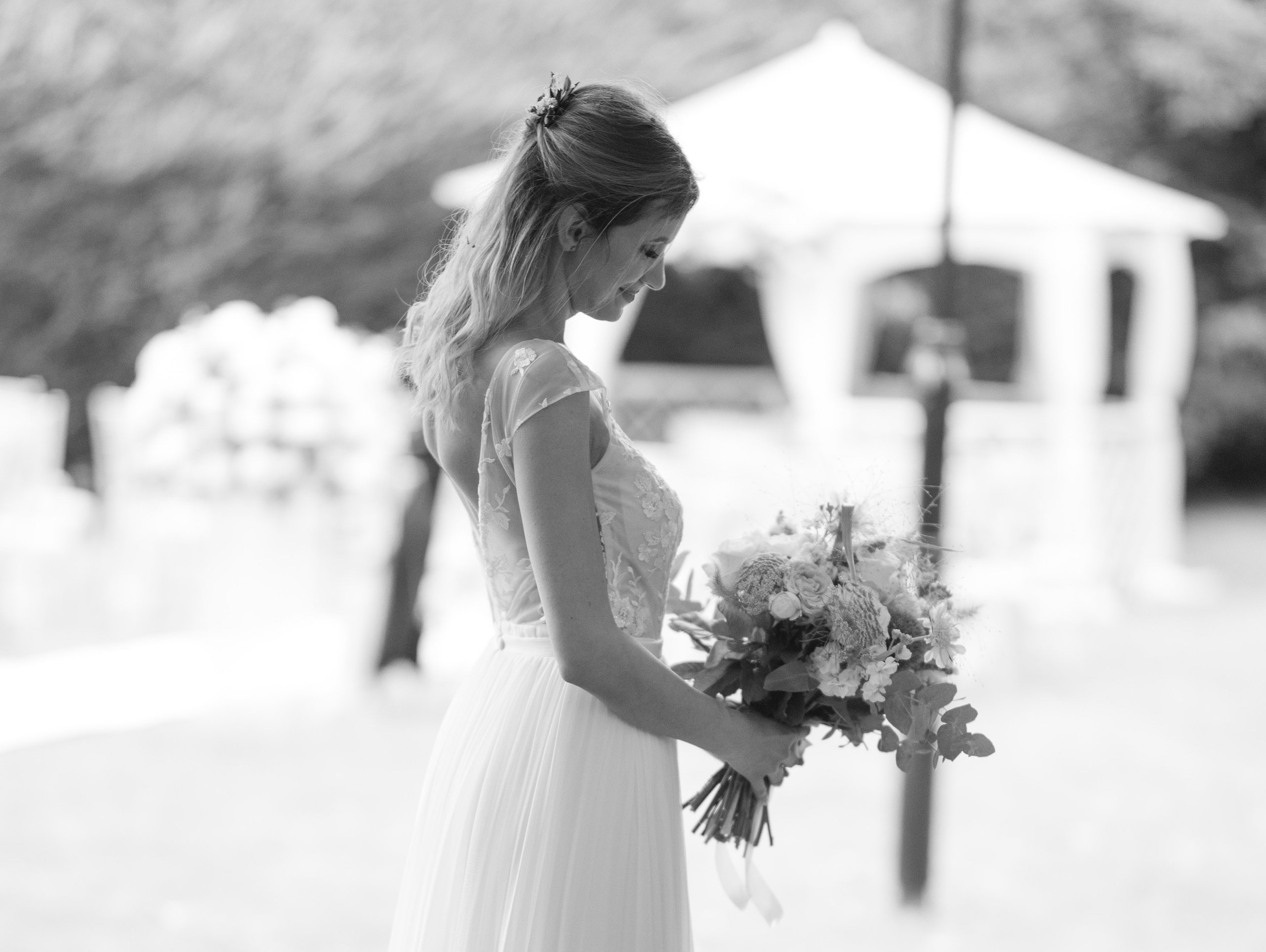 Bride looking down at her bouquet in profile, soft garden light (black and white)