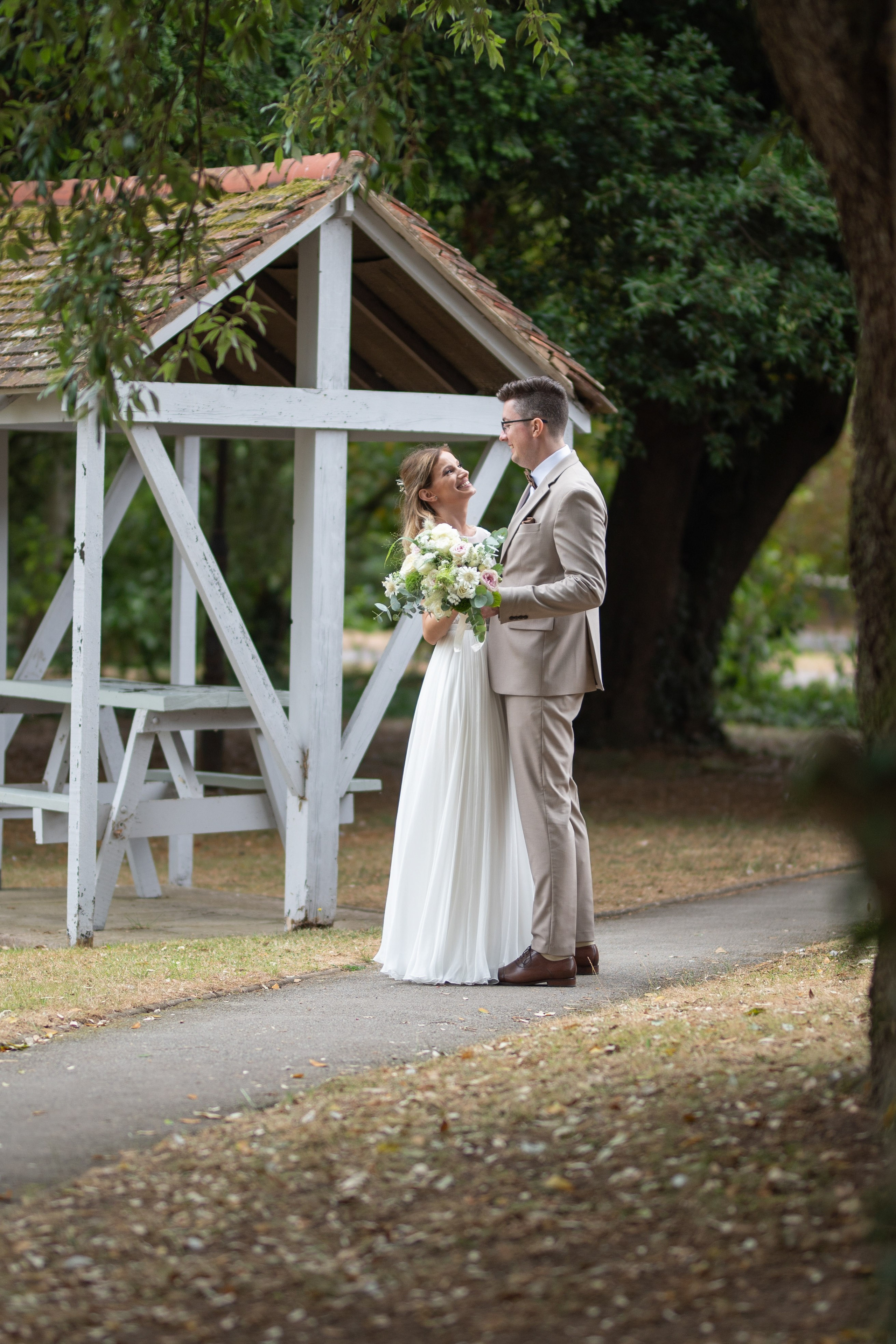 Bride and groom laughing together by the white wooden garden shelter