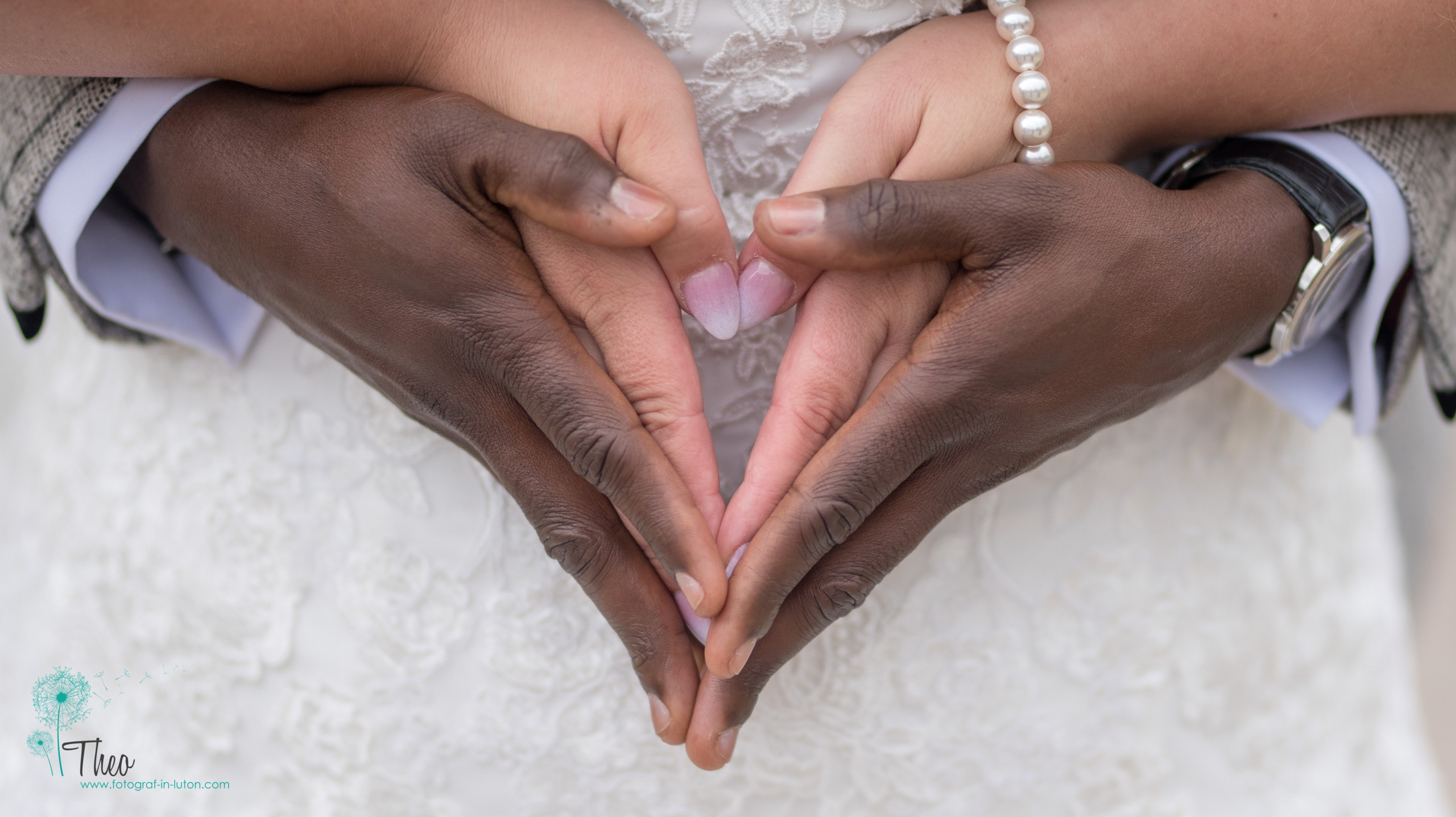 The bride and groom's hands form a heart shape, her pearl bracelet catching the light