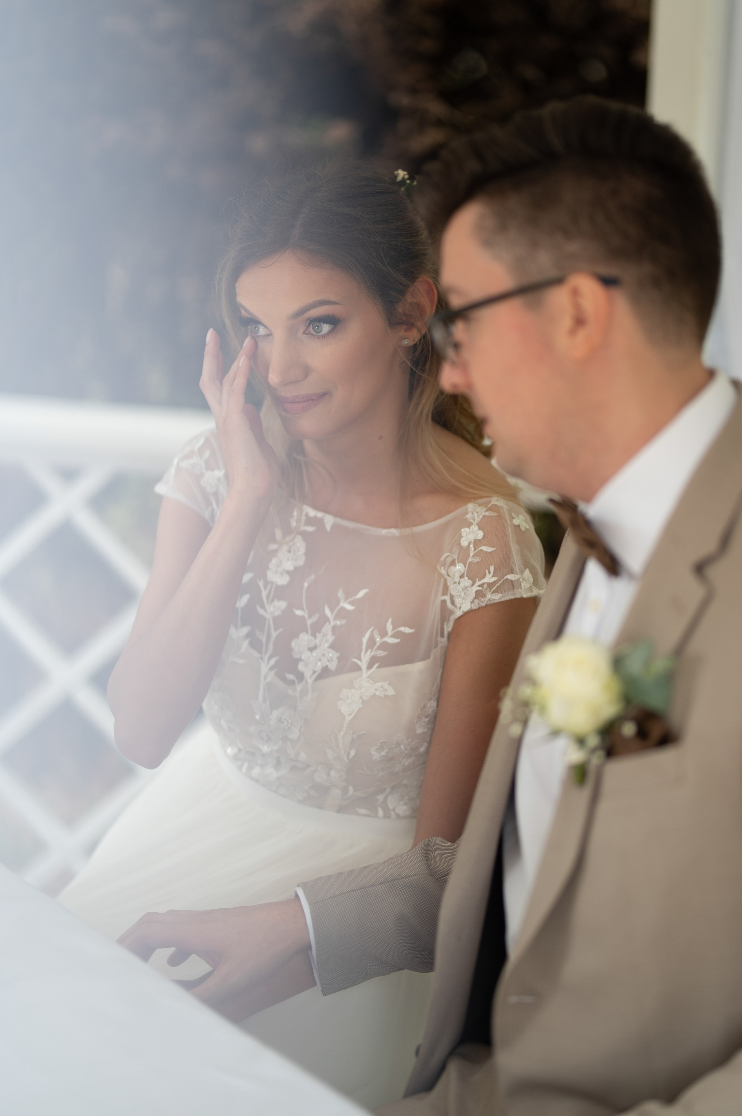 Close-up of the bride wiping away a happy tear during the ceremony, groom beside her