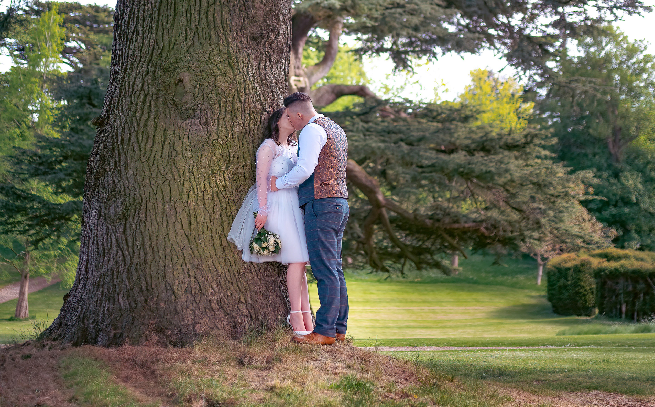 Bride and groom embracing against a large tree trunk at Luton Hoo