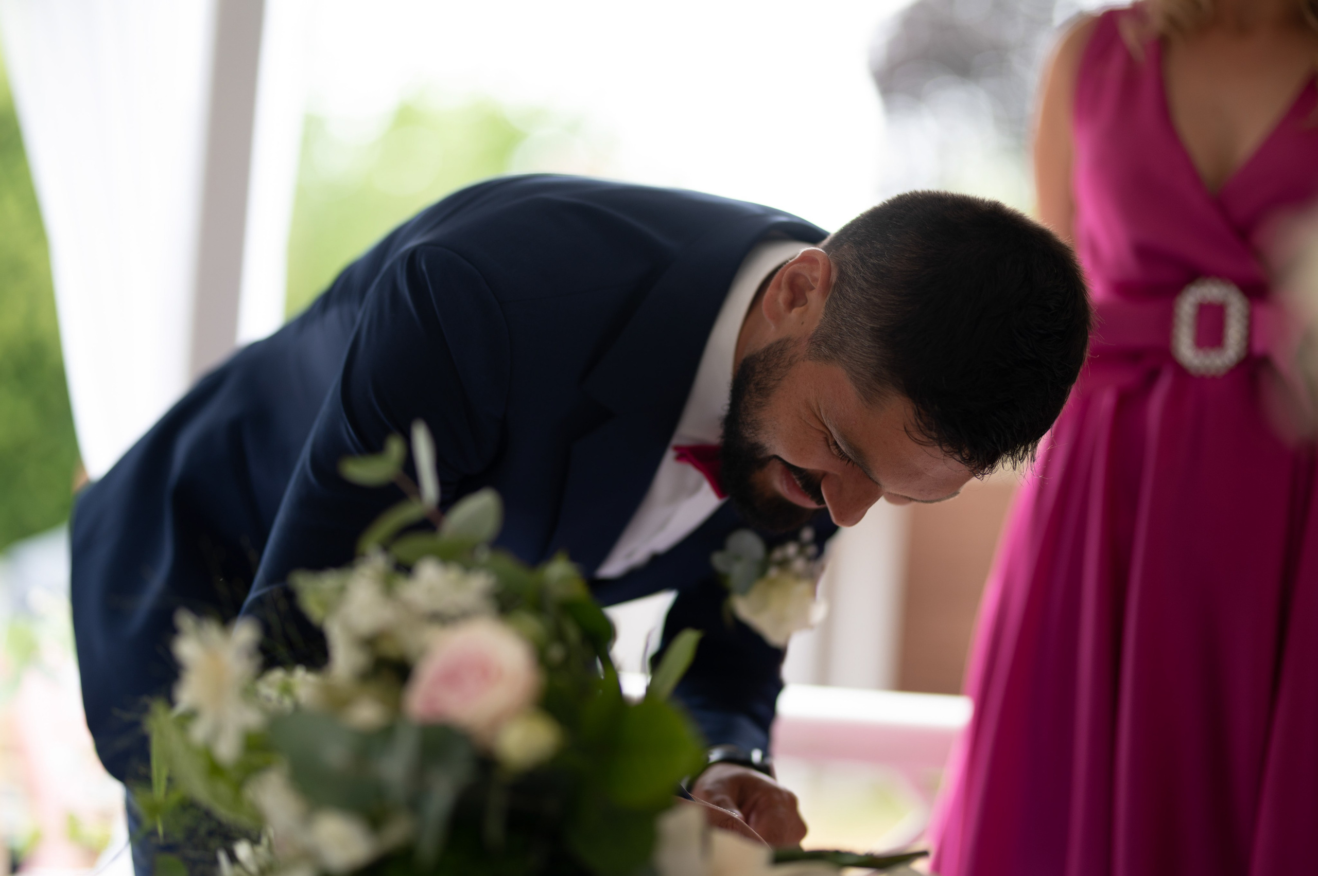Groom signing the wedding register at Charlecote Pheasant Hotel, bridesmaid in magenta dress alongside