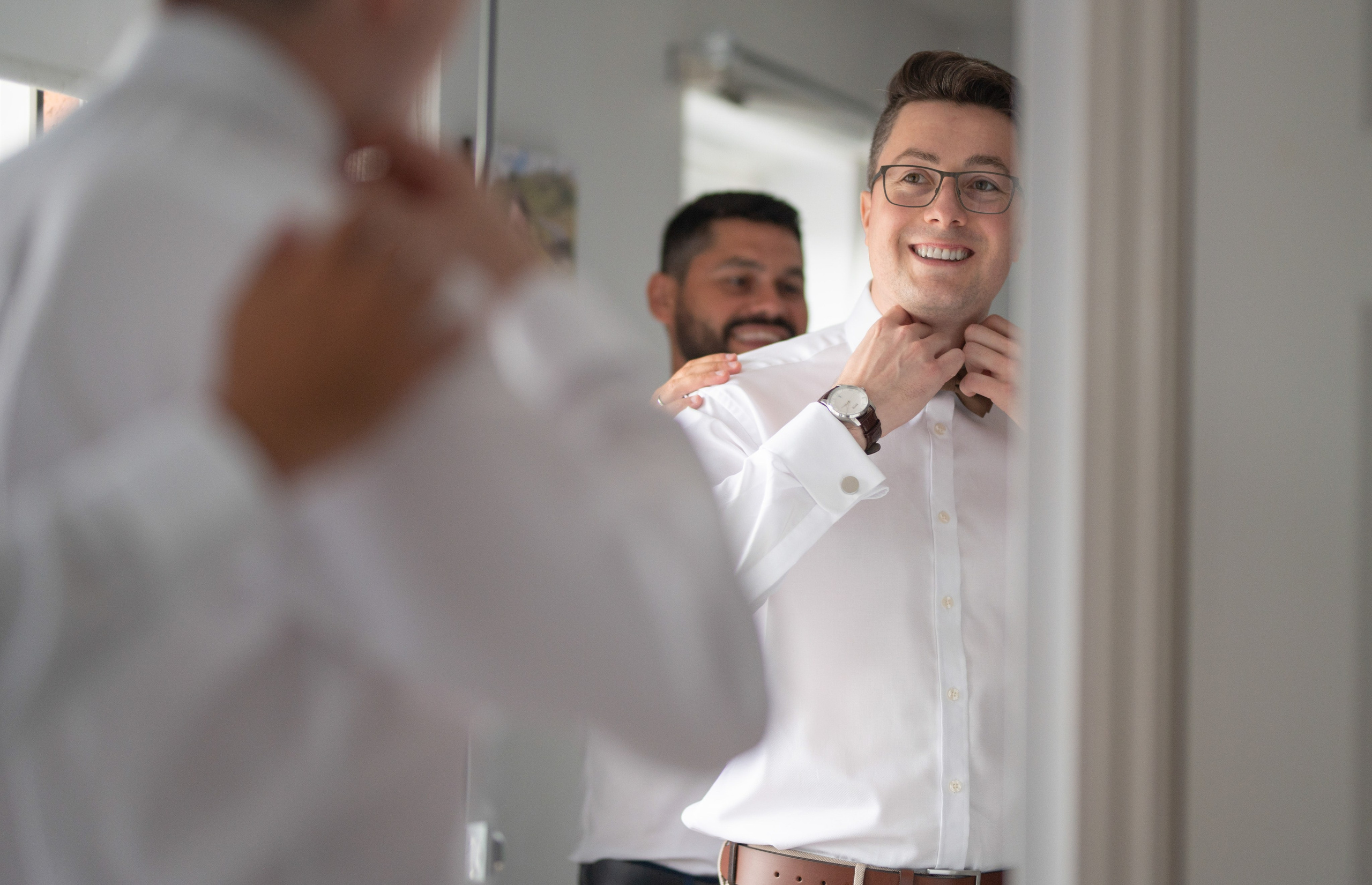 Groom smiling as a groomsman helps him get ready, Charlecote Pheasant Hotel
