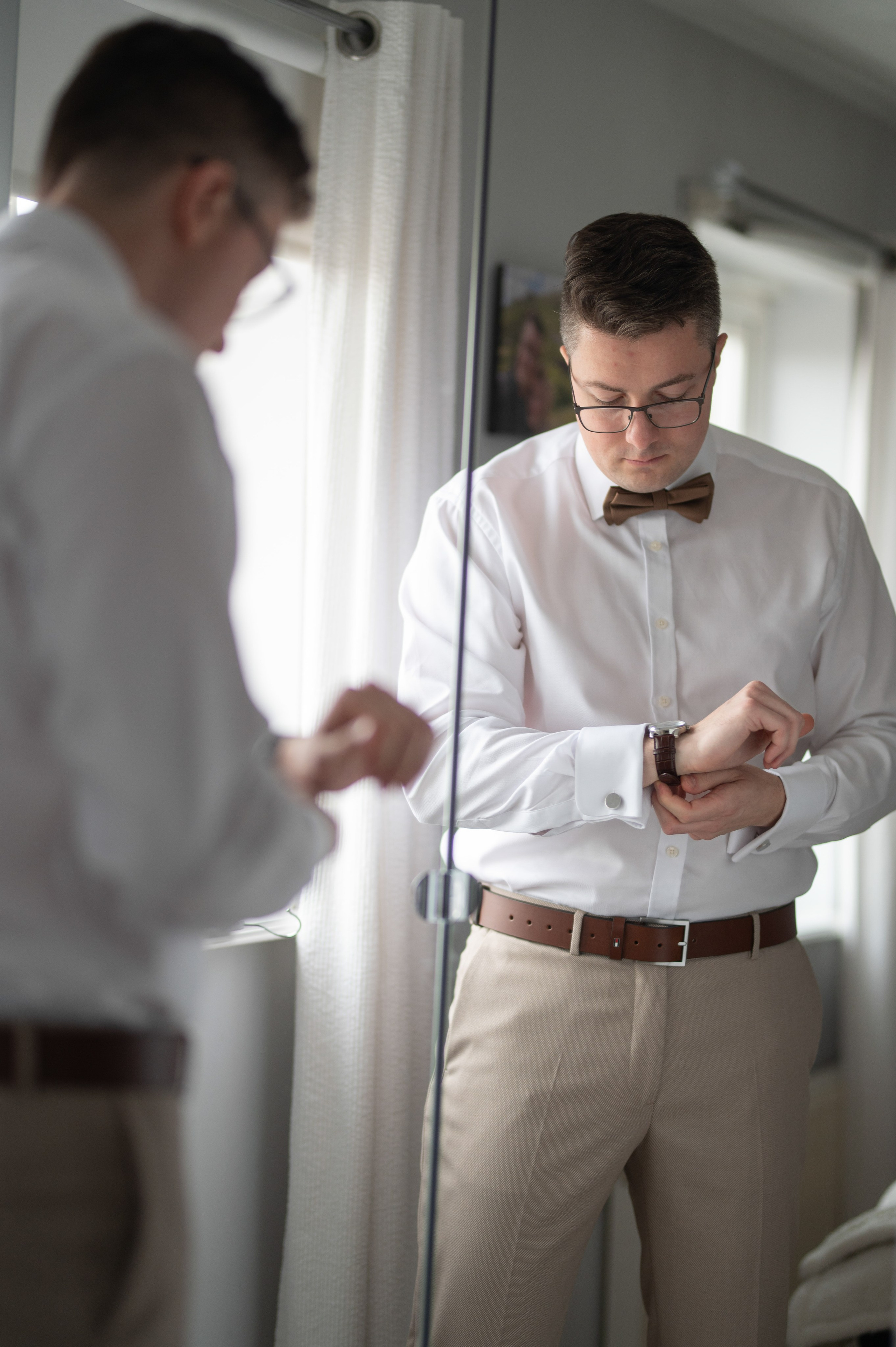 Groom adjusting his watch and cufflinks in the mirror while getting ready, Charlecote Pheasant Hotel