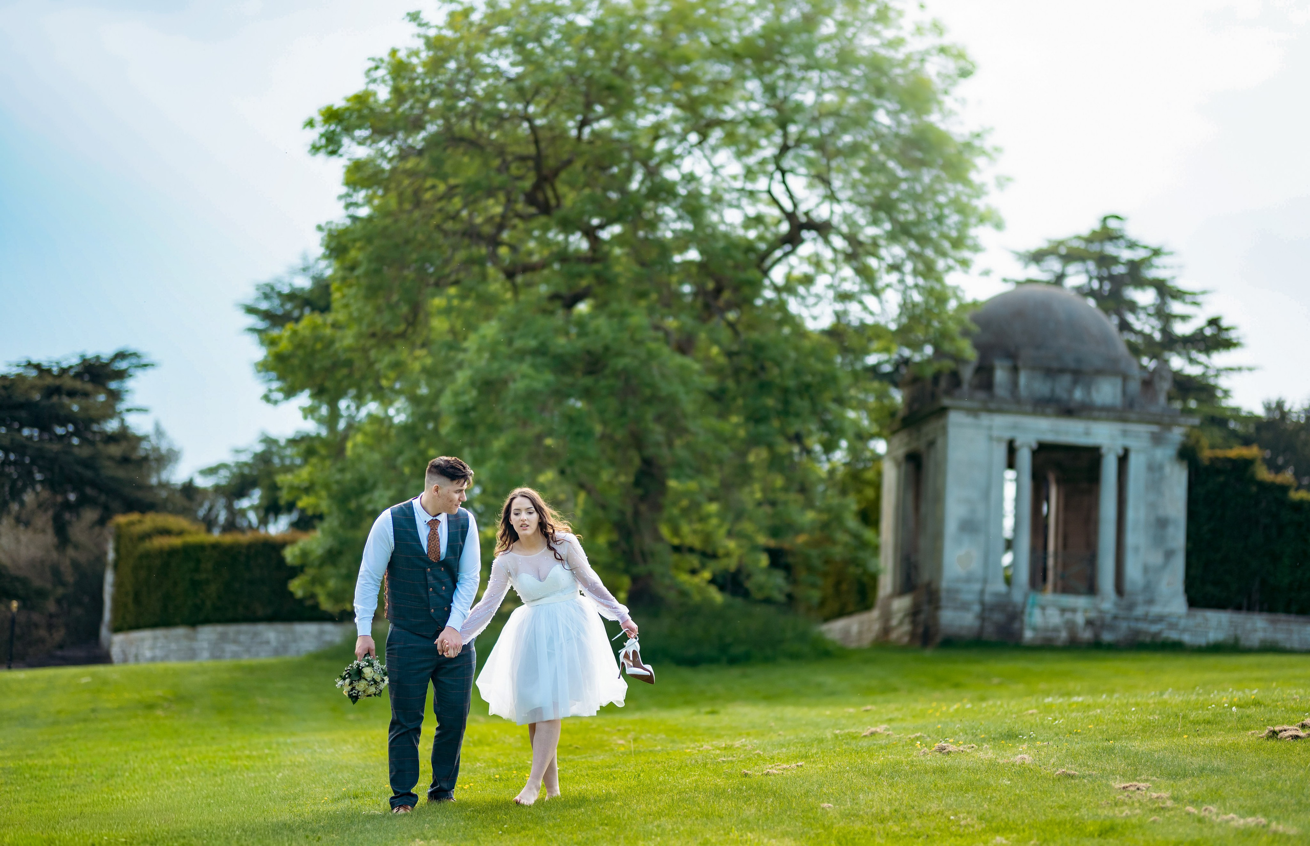 Bride and groom walking across the lawn near a large tree at Luton Hoo