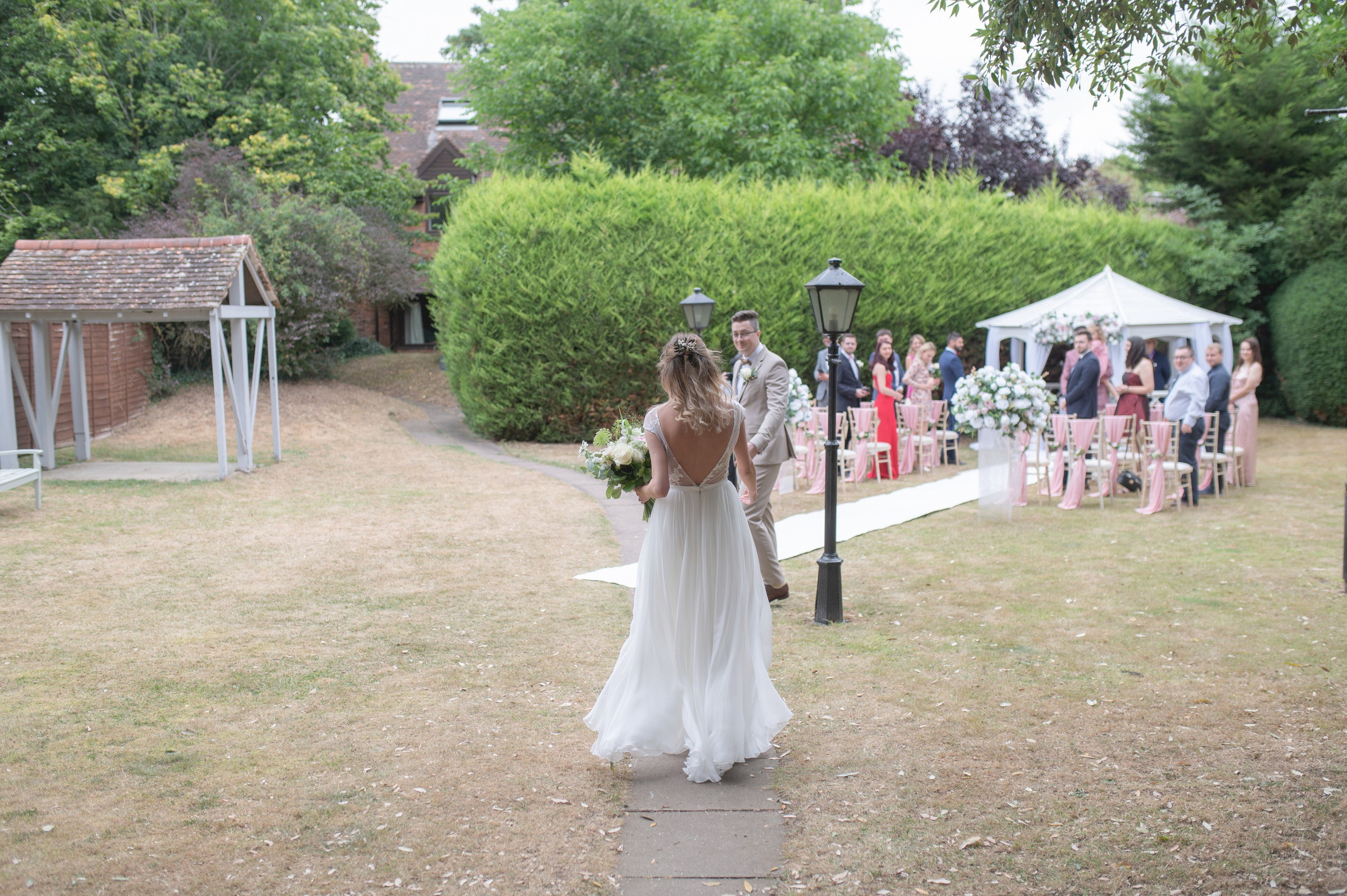 Bride walking down the garden aisle with her father towards the outdoor ceremony at Charlecote Pheasant Hotel