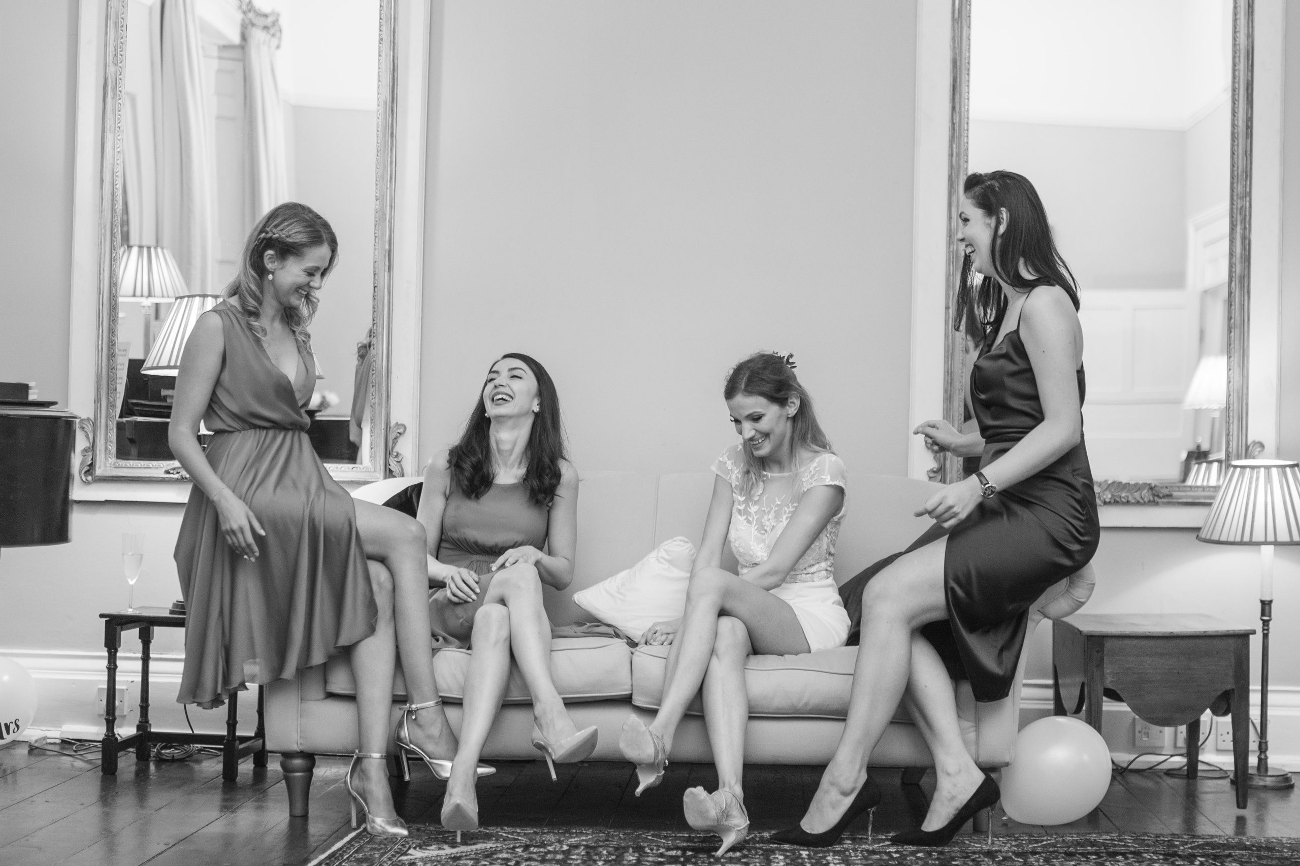 Bride and bridesmaids laughing together on the sofa, evening reception (black and white)