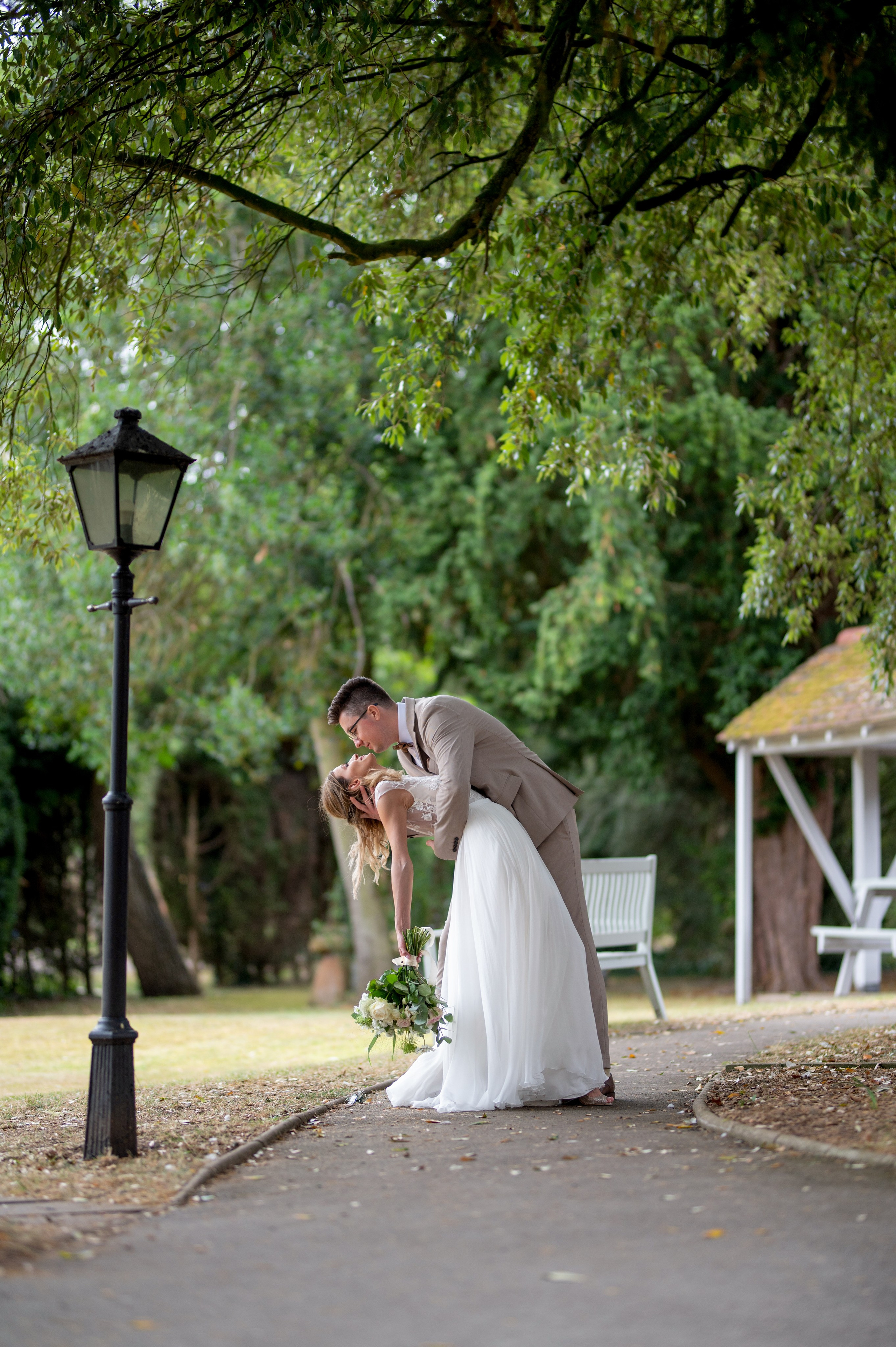 Romantic dip kiss between the newlyweds under the trees at Charlecote Pheasant Hotel, vintage lamp post nearby