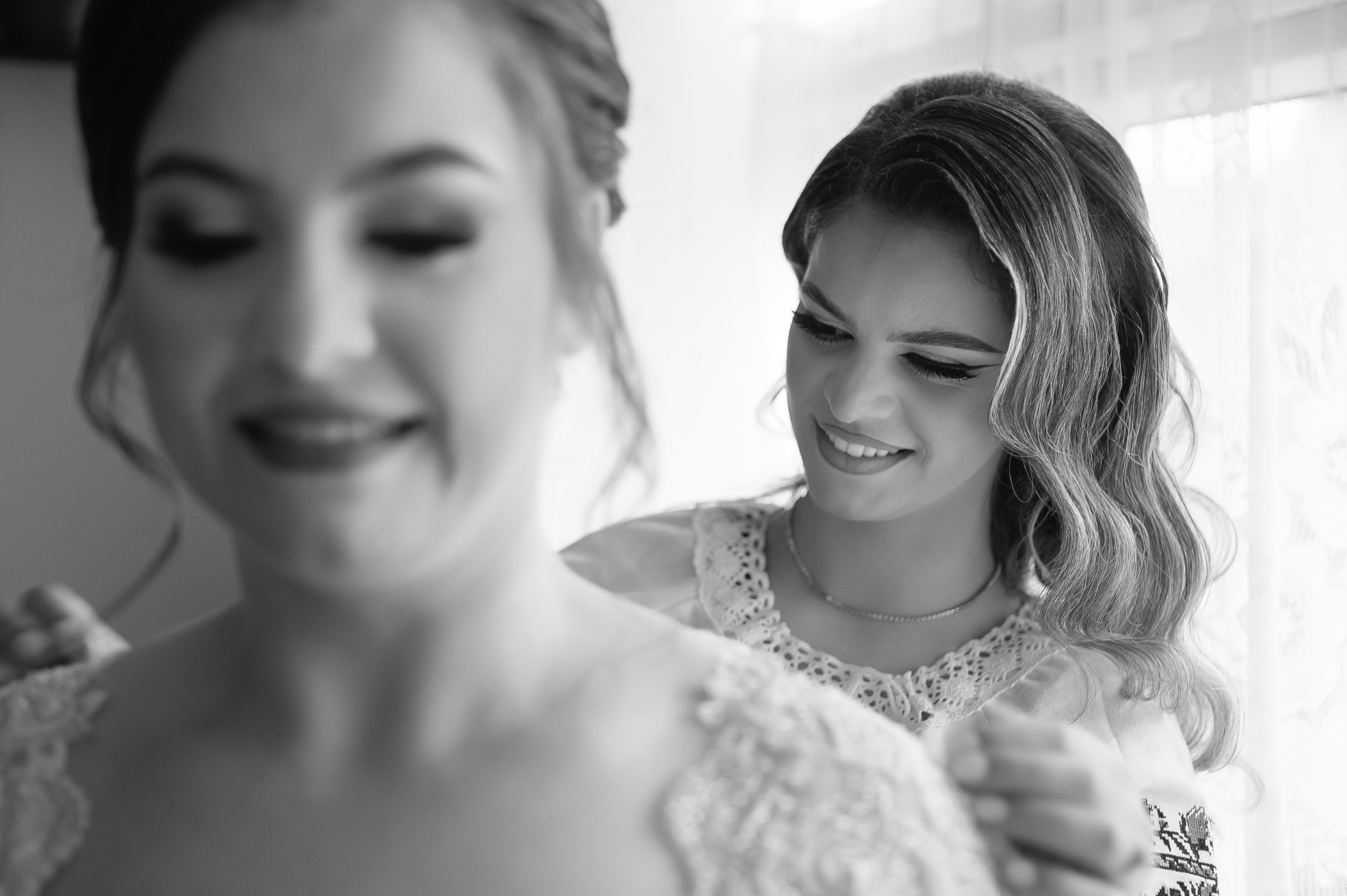 Bride sharing a tender moment with a bridesmaid adjusting her hair, black and white