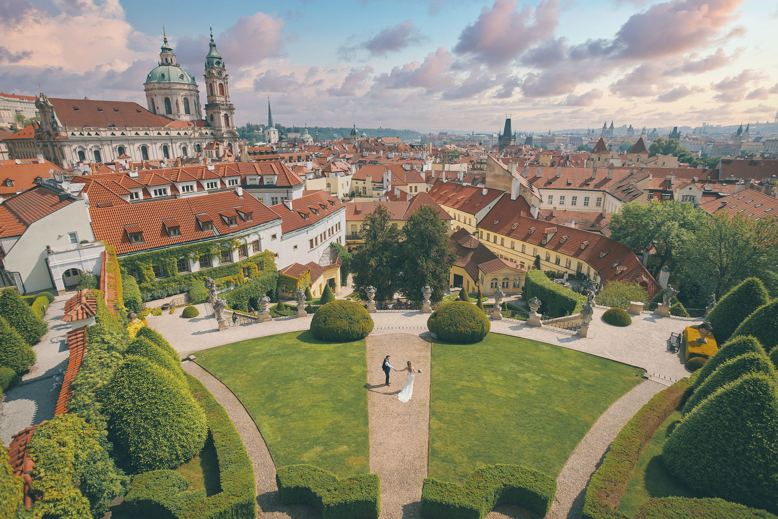 Solitary bride and groom walk through the landscaped gardens of the Vrtba Garden as seen from above