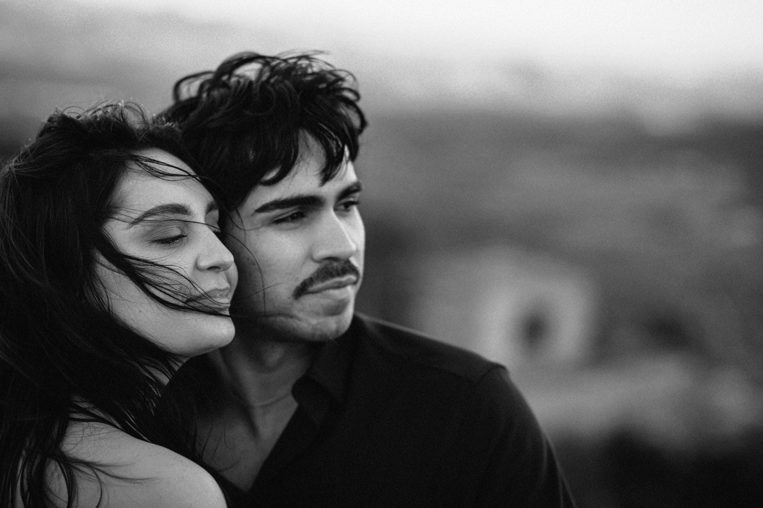 Close-up portrait of bride and groom embracing in the mountains during an intimate destination wedding in Barcelona, Spain. Wind-blown hair and soft light create a cinematic elopement atmosphere perfect for a romantic engagement session.
