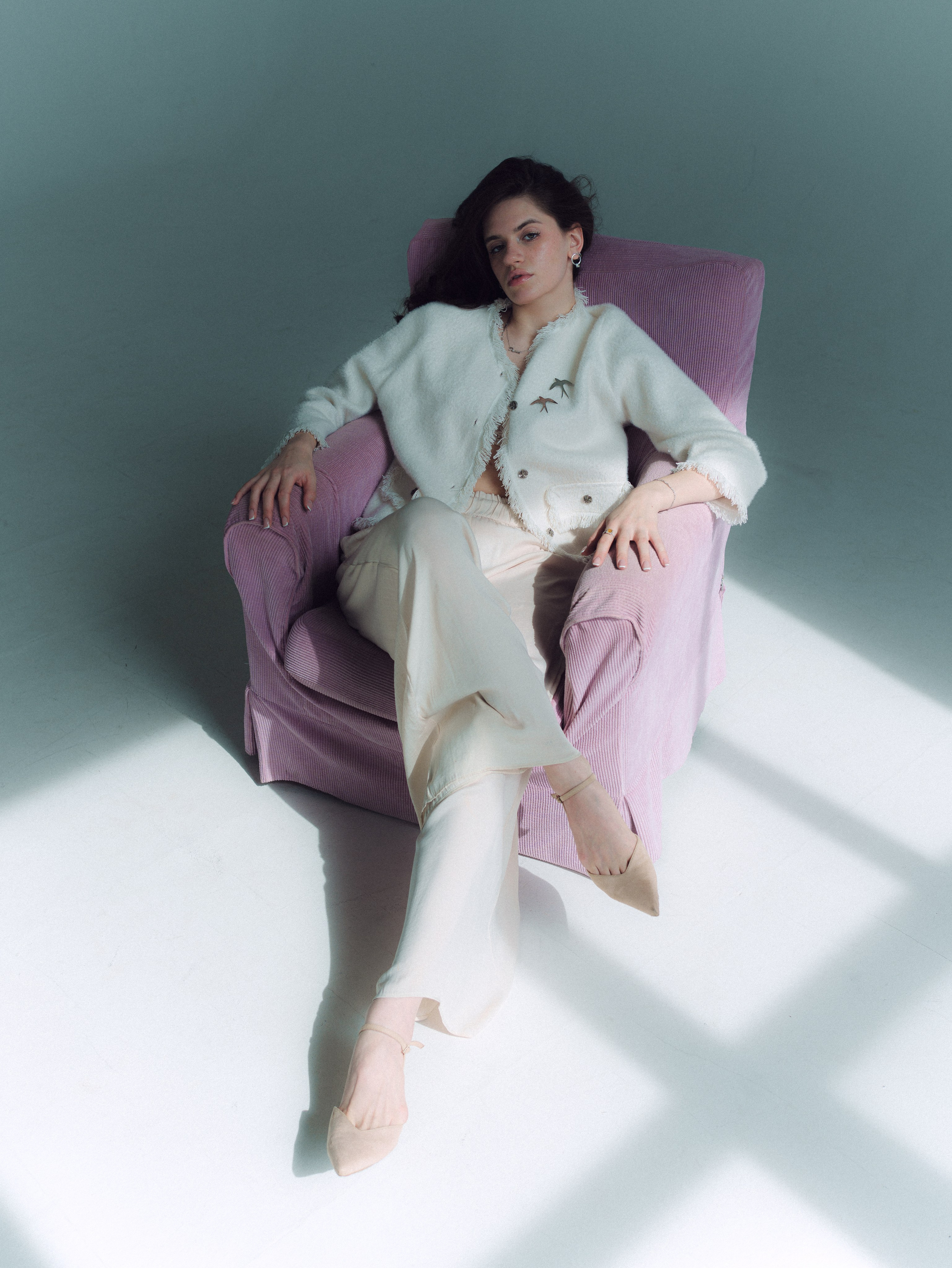 Woman sitting in pastel chair with soft daylight and white minimal background