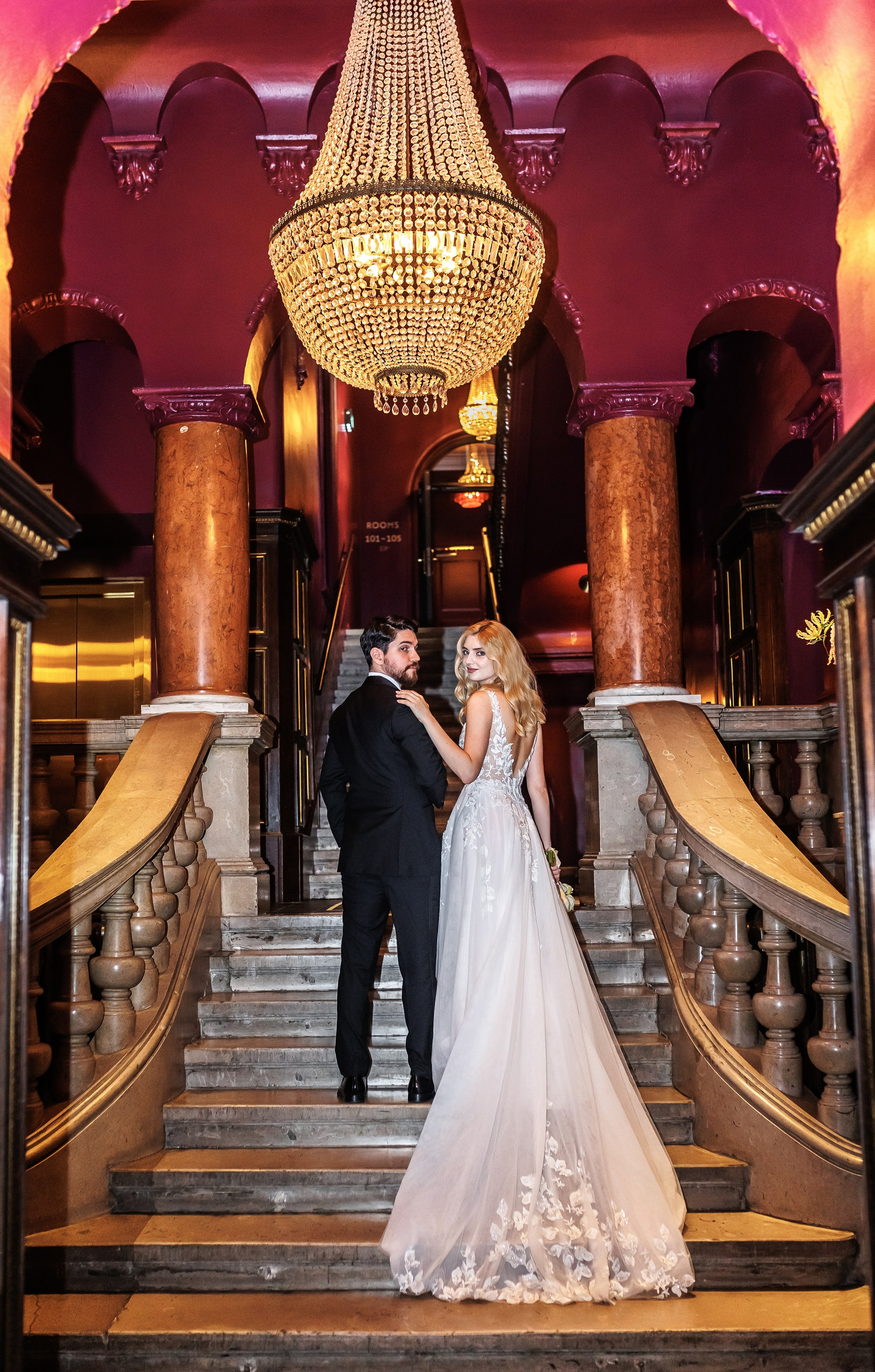 Brautpaar auf festlicher Treppe mit goldenem Kronleuchter – Editorial Hochzeit Berlin | Nataliia Schütze 