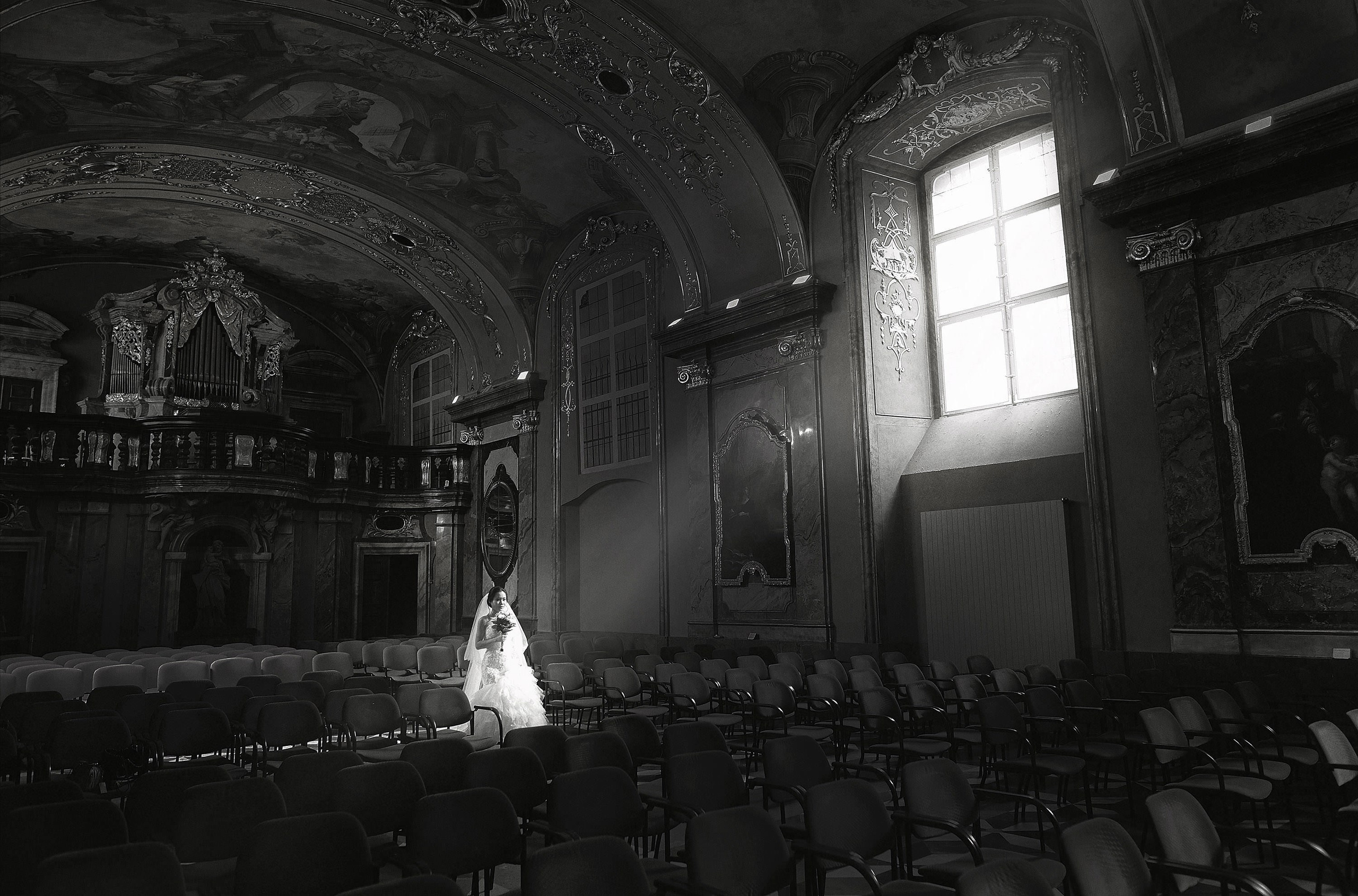 Black and white photo of Chinese bride in Mirror Chapel, Klementinum, Prague, with light from a single window