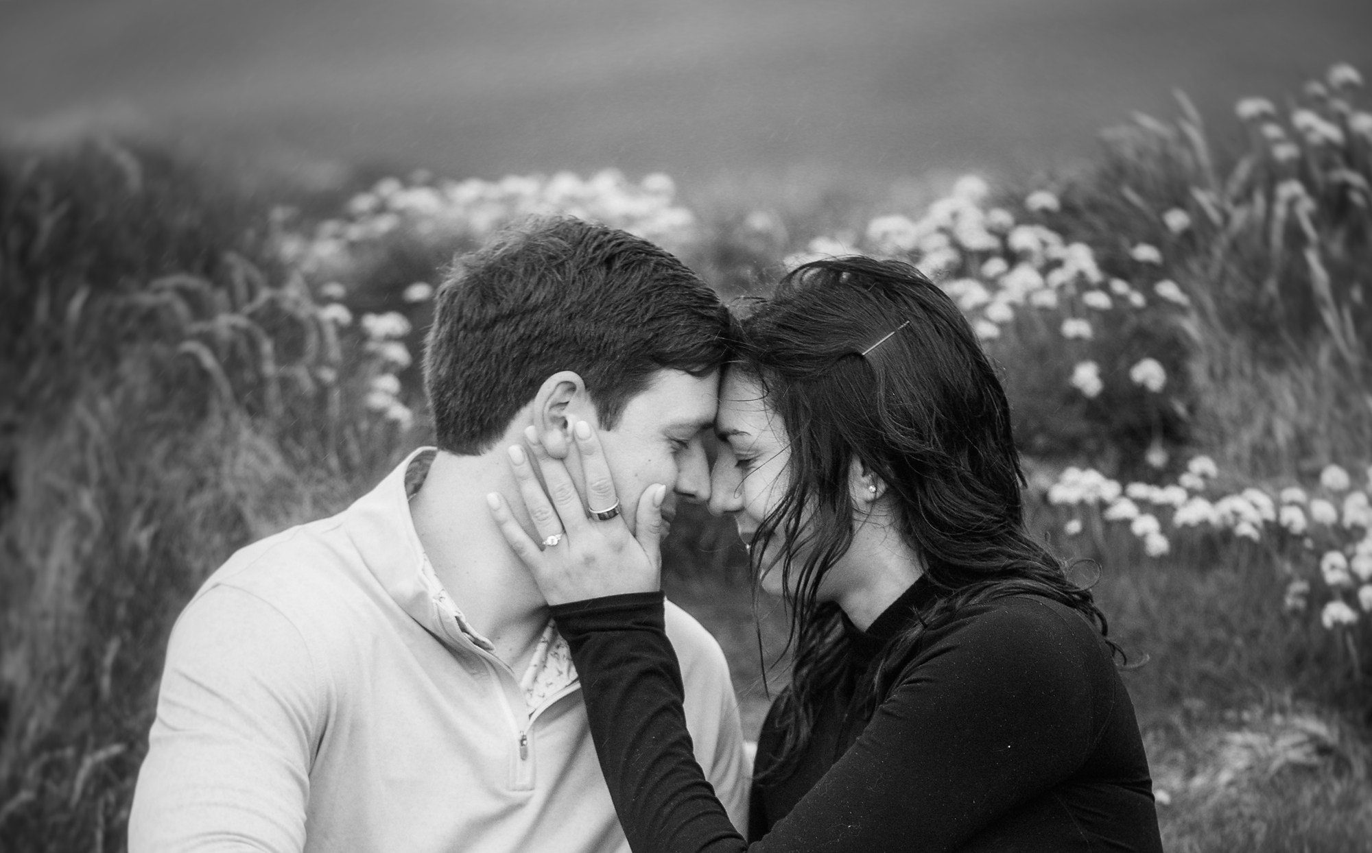 Black and white portrait of a happy couple sitting in a flower-filled meadow, captured during a photoshoot in Dublin.