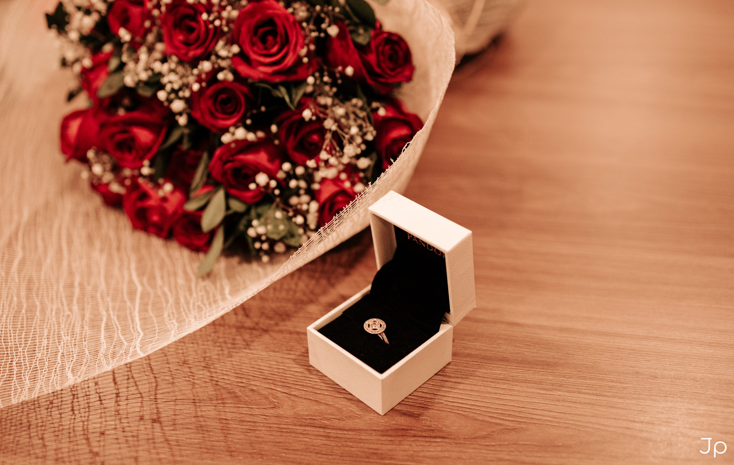 Caixa com aliança ao lado de buquê de rosas vermelhas.