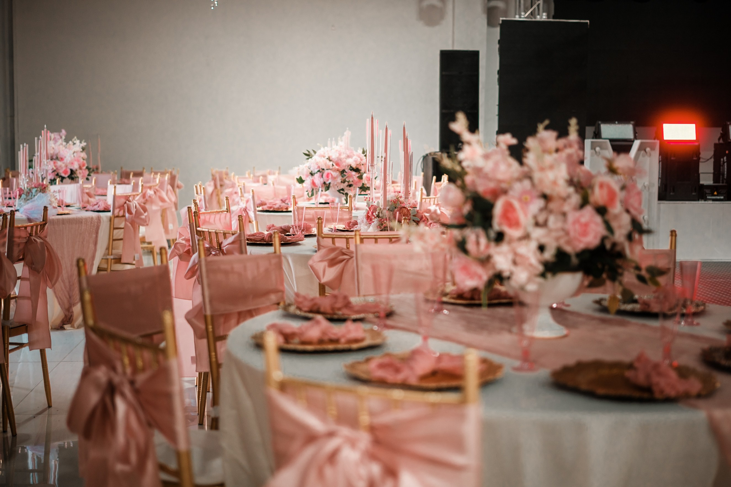 Spacious ballroom reception setup featuring round banquet tables decorated in blush pink and gold