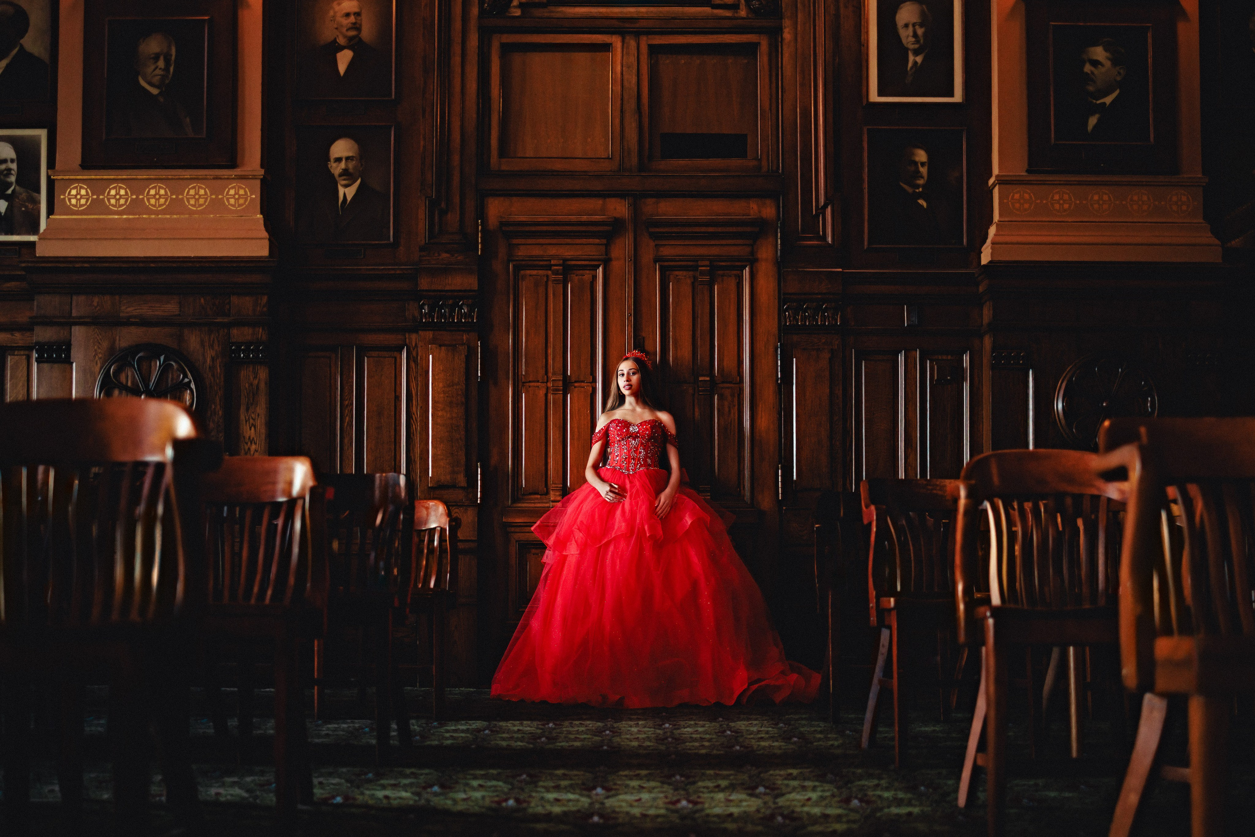 Dramatic quinceañera portrait in red dress inside classic wood library interior