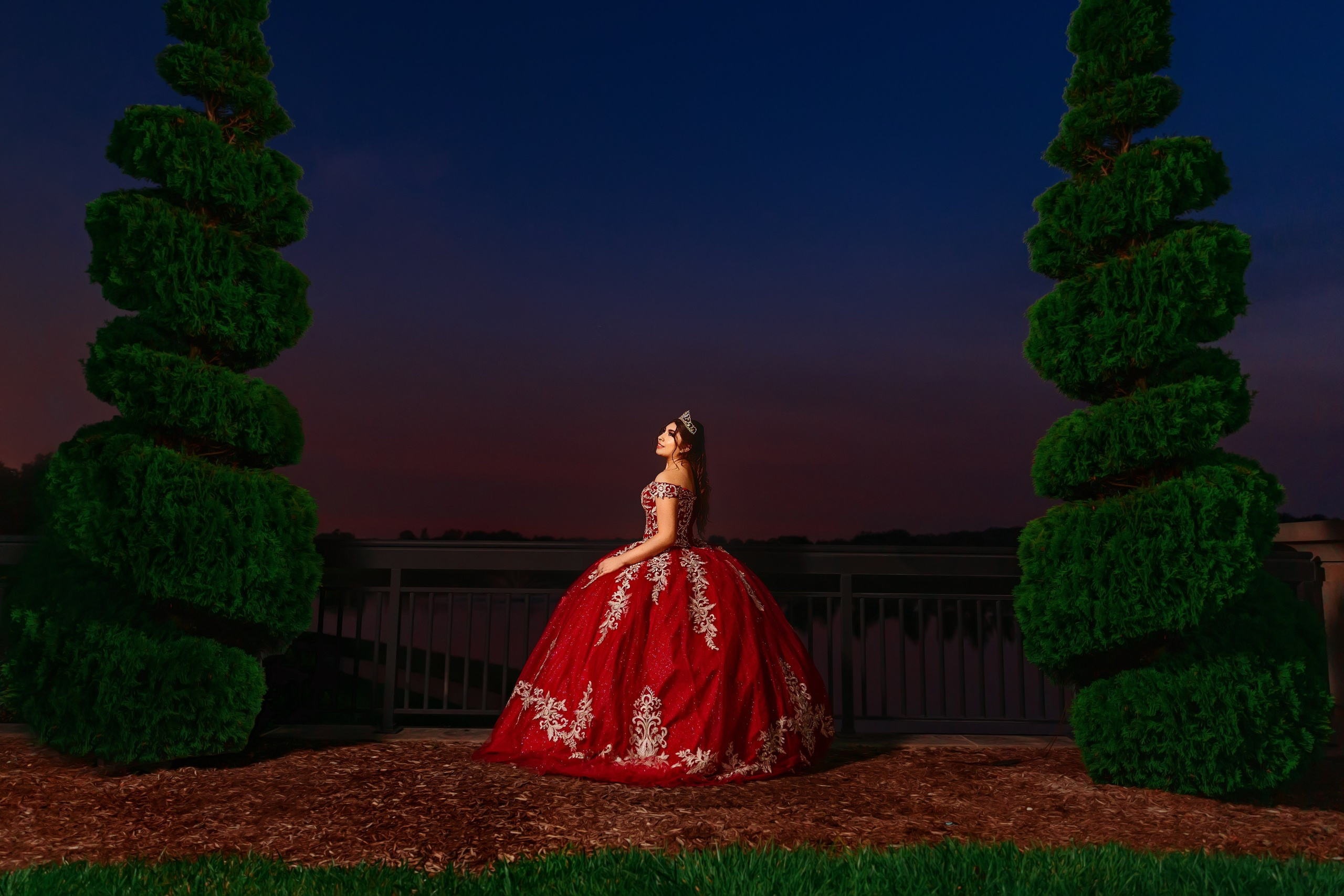 Outdoor quinceañera portrait session at dusk with red gown and lush landscape