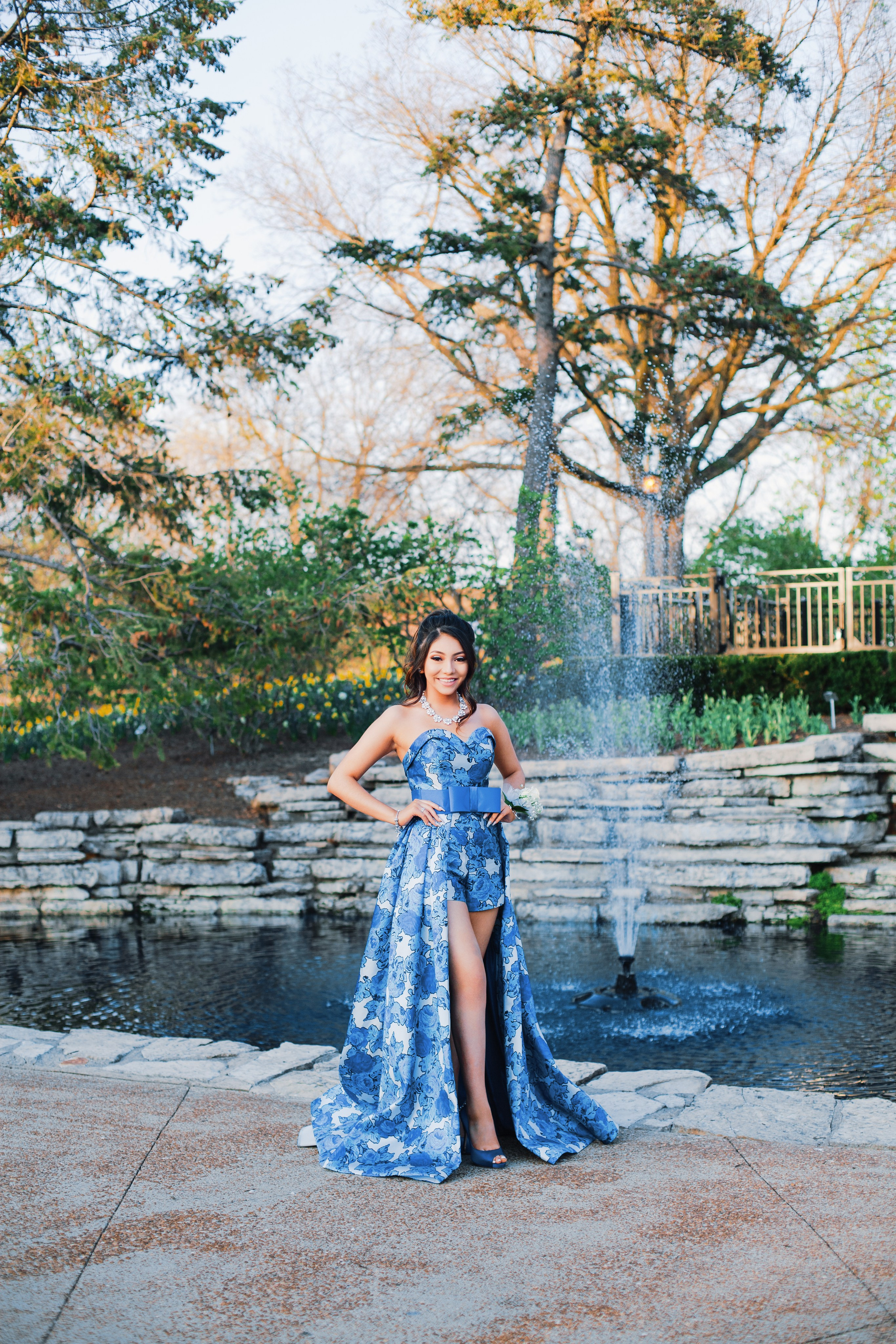 Elegant milestone portrait of young woman in royal blue dress by fountain in Indianapolis
