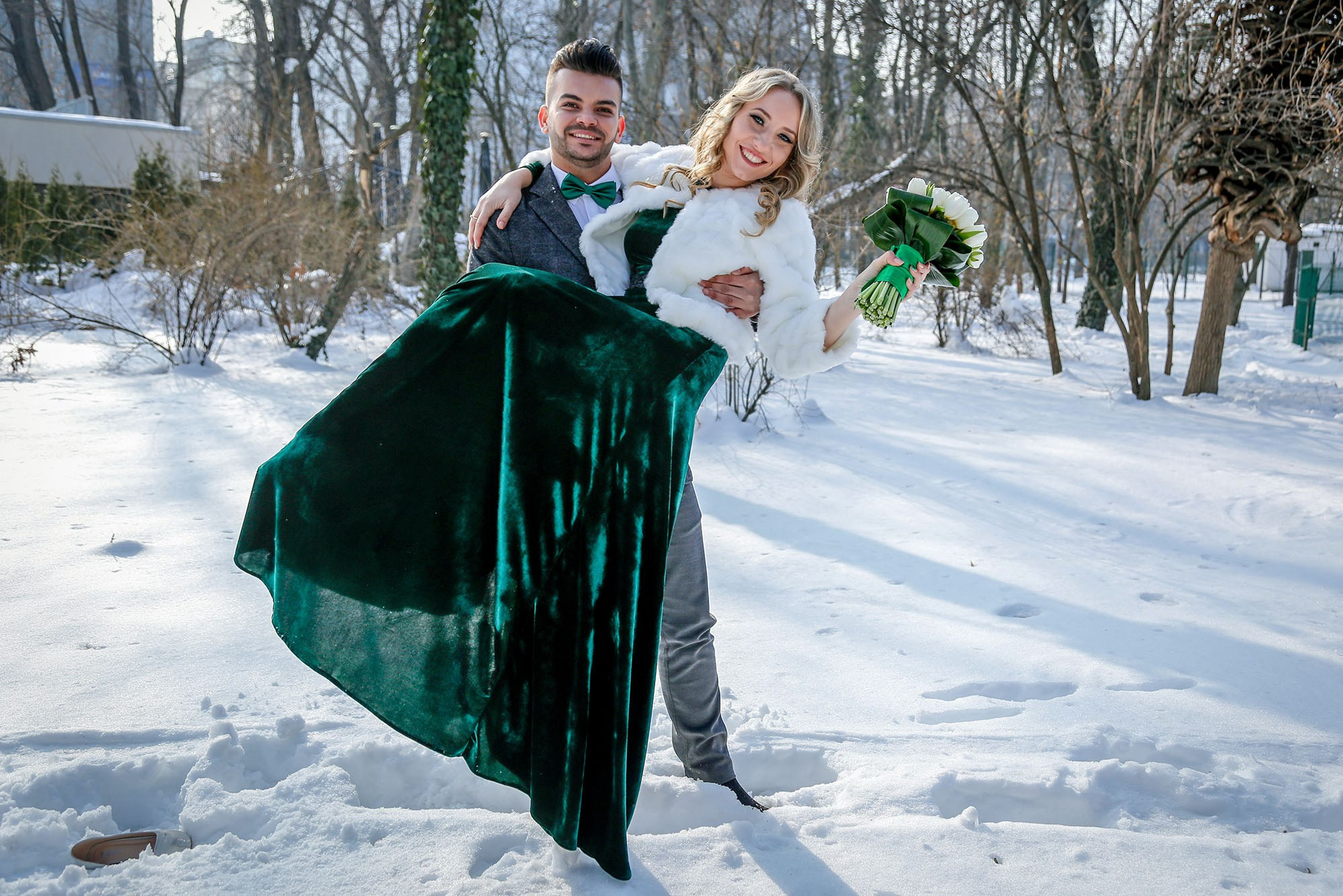 The groom joyfully lifting the bride in his arms amidst the snow, a romantic and energetic winter wedding photo.