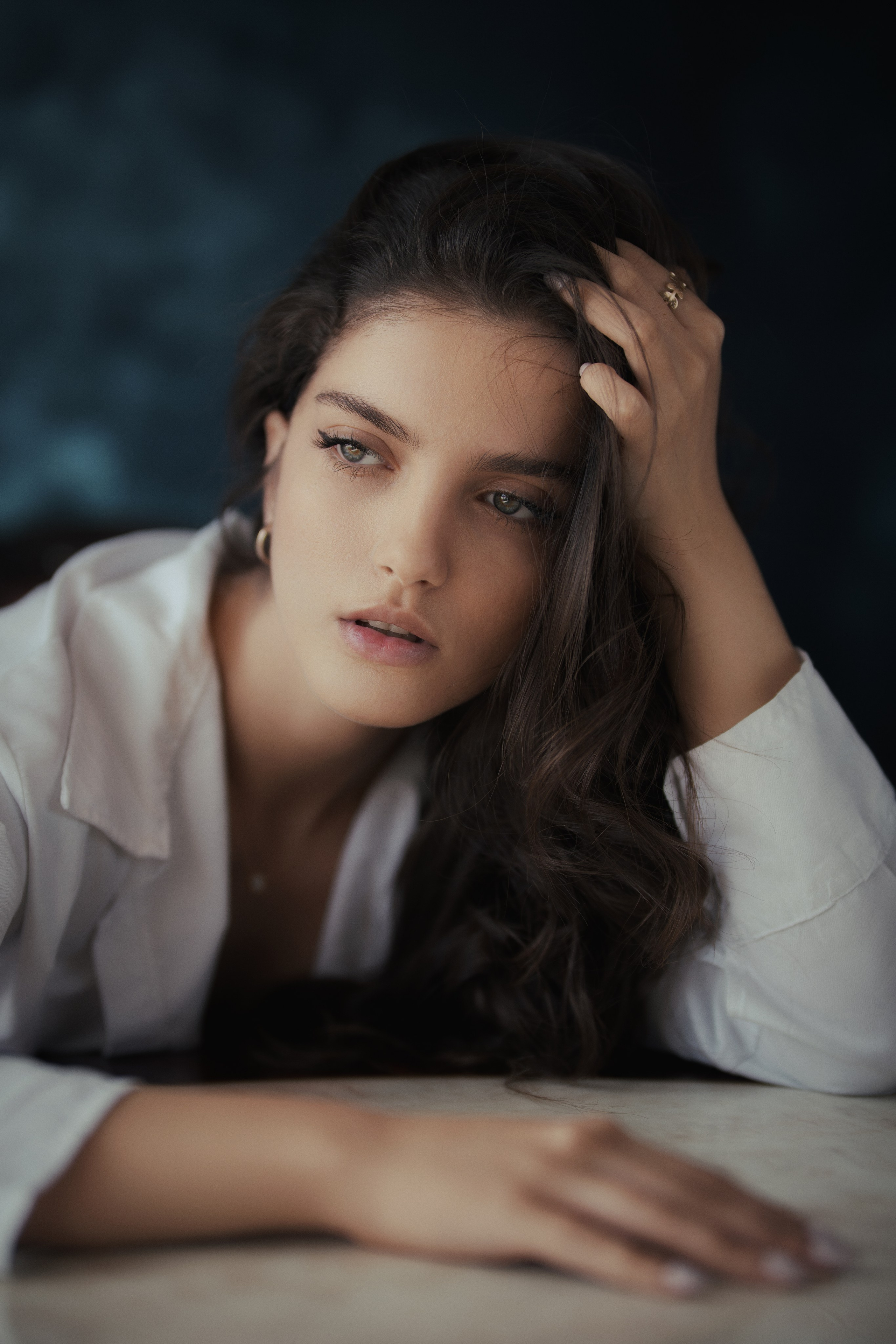 Fine art female portrait photography by Mehran Hadad featuring a young woman in a white shirt with soft cinematic lighting and a textured blue studio backdrop.