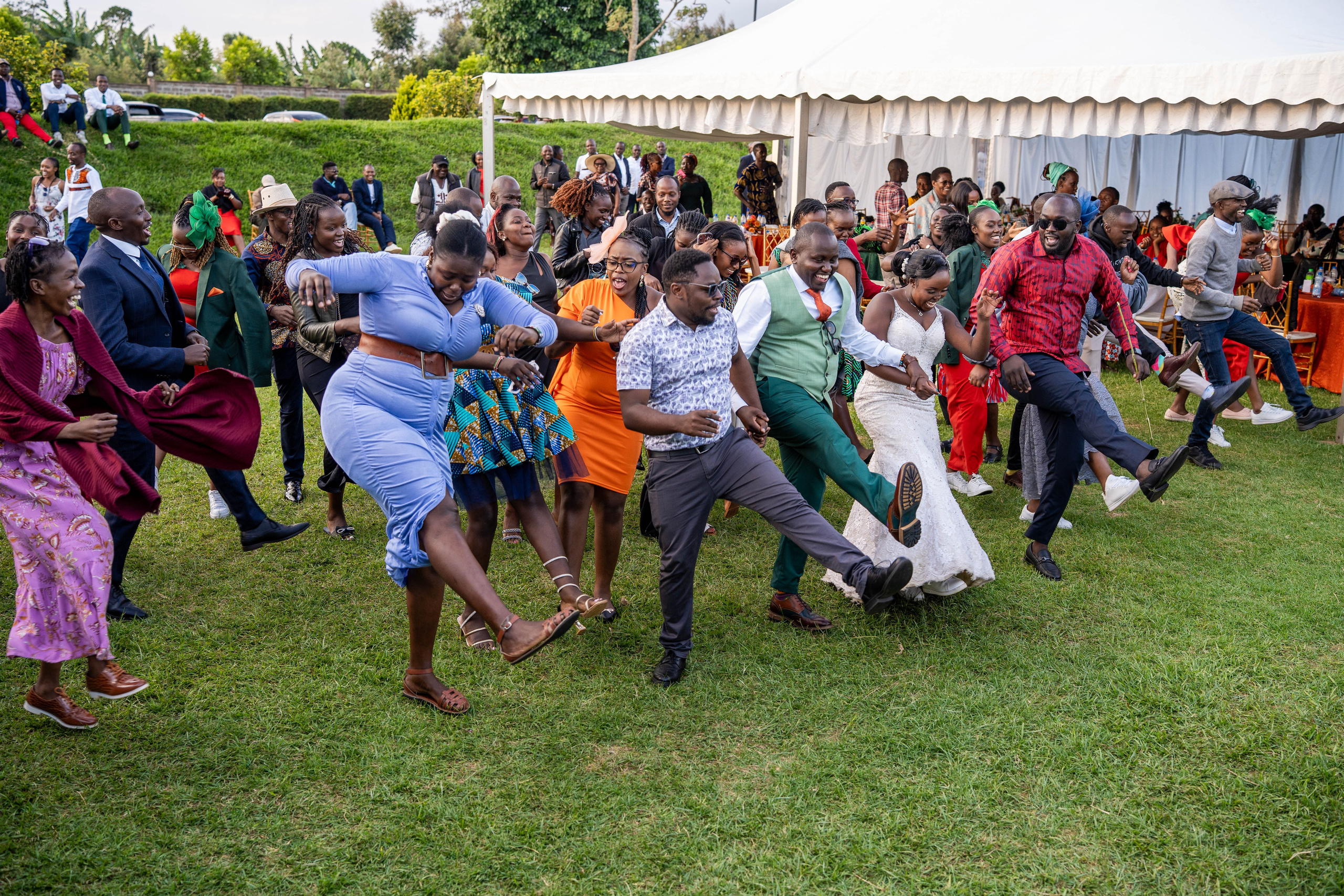 A group of wedding guests dancing together with the bride and groom at an outdoor reception
