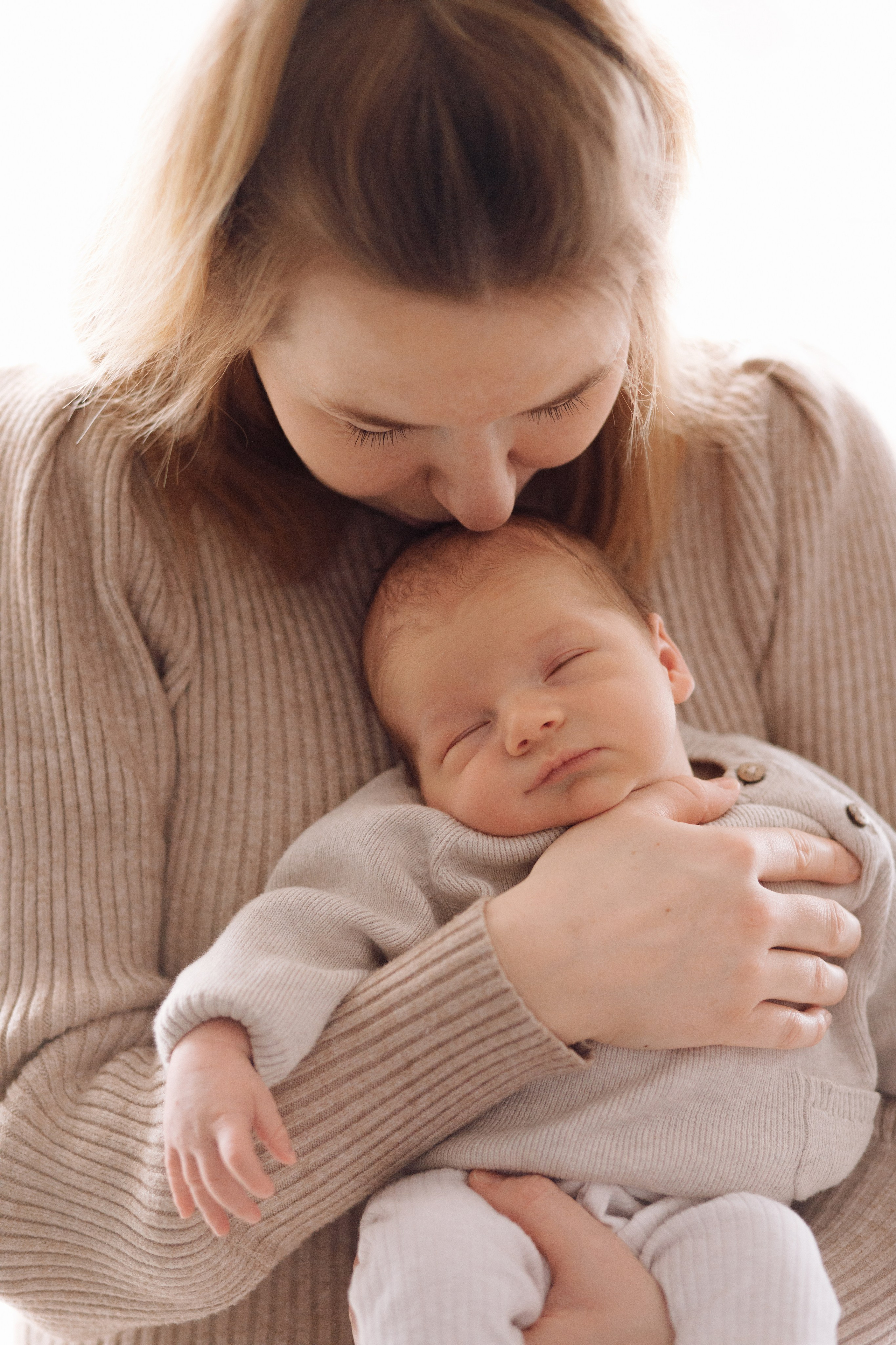 Mutter hält ihr Baby und küsst es sanft auf die Stirn.