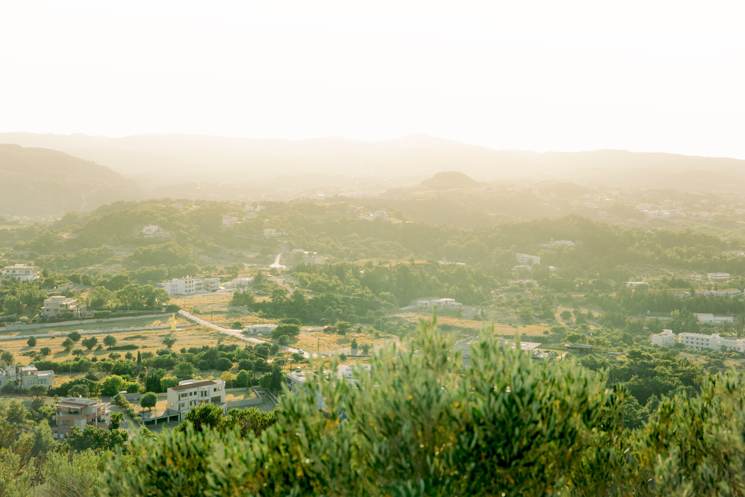 "Panoramablick vom Gipfel des Profitis Ilias über die Bucht von Faliraki. Im Vordergrund ein frisch verlobtes Paar vor der weißen Kapelle, umgeben von der kargen, mediterranen Schönheit der griechischen Inselwelt."