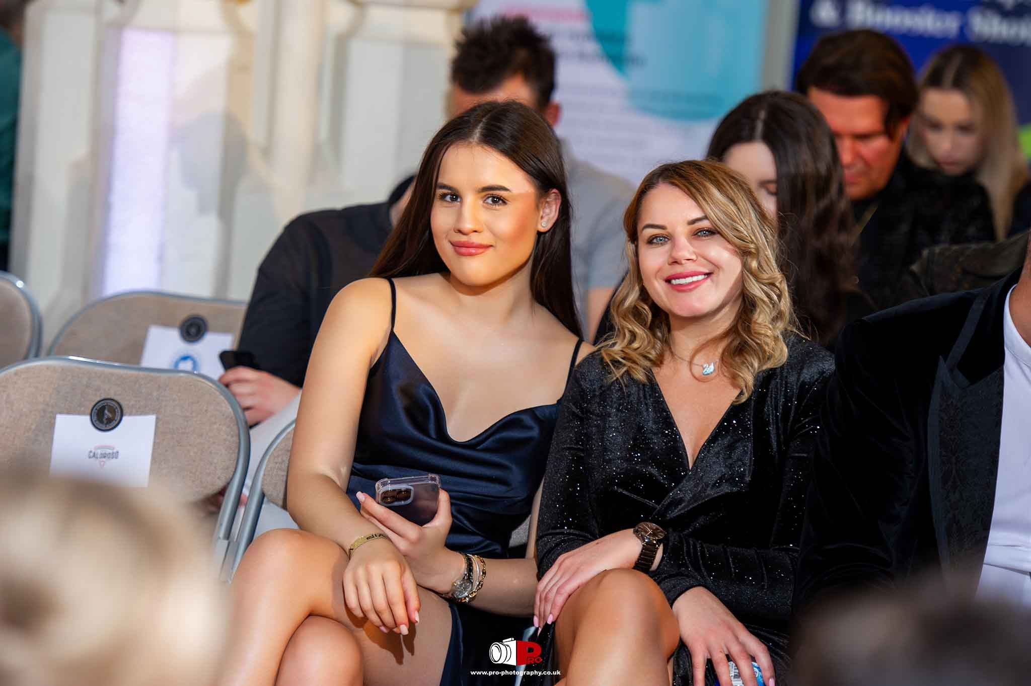Two stylish women in black dresses smiling at the camera during a formal event.