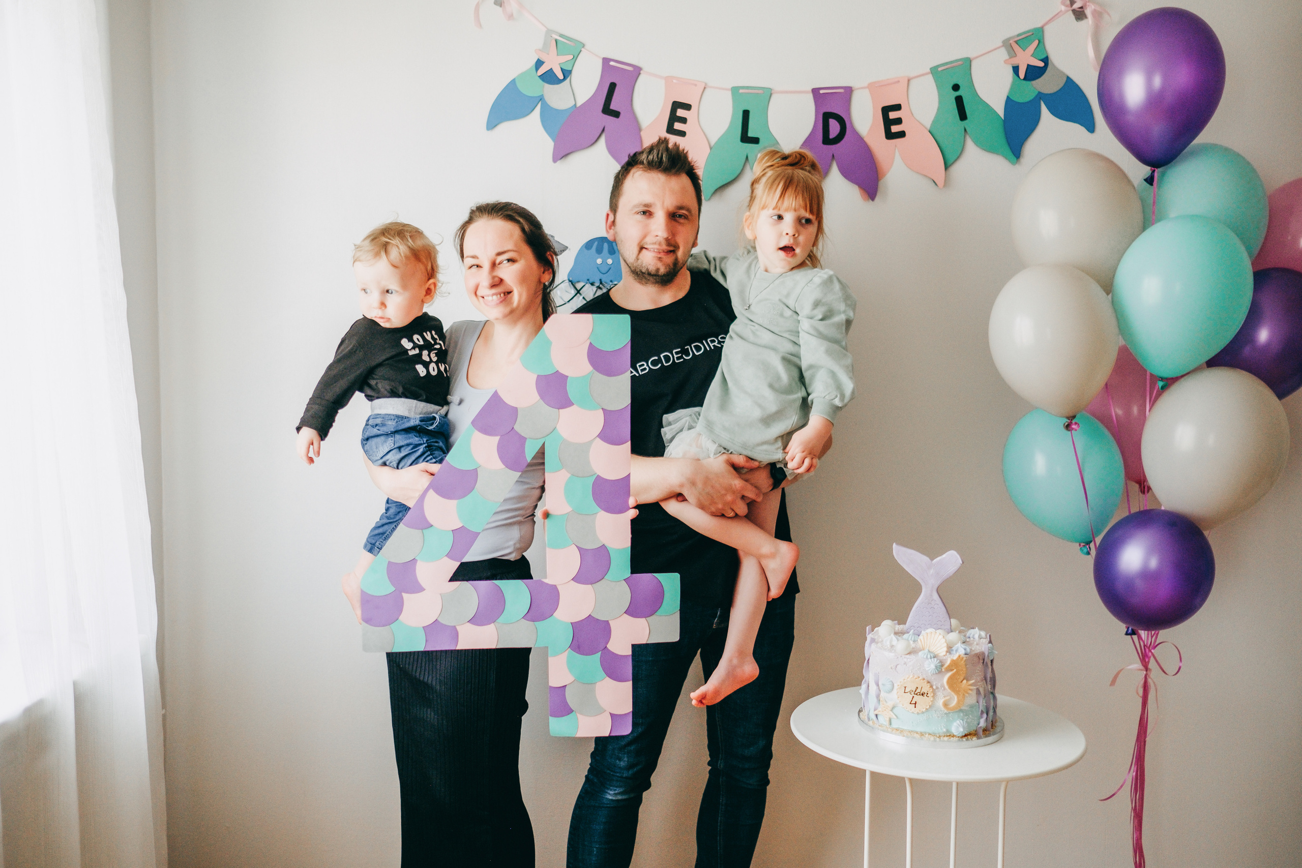 Privātās ģimenes fotosesijas, bērnu dzimšanas dienas ballītes foto. Ģimenes bilde ar diviem bērnie, mammu un tēti pie dekorētas sienas "nāriņas ballītes" tēmā. 