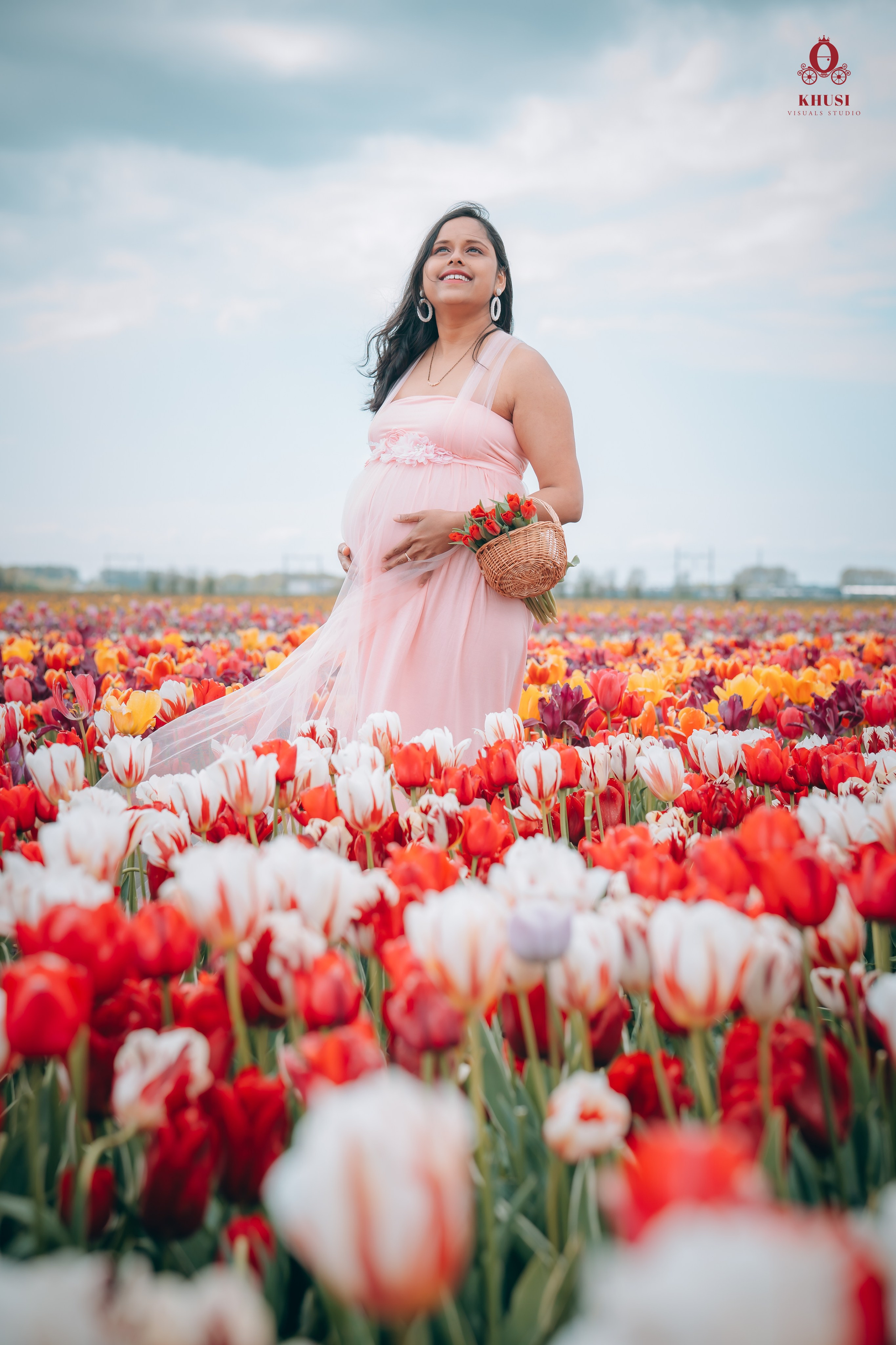 A pregnant woman standing in a tulip fields in netherlands with white and red tulip flowers and enjoying the view