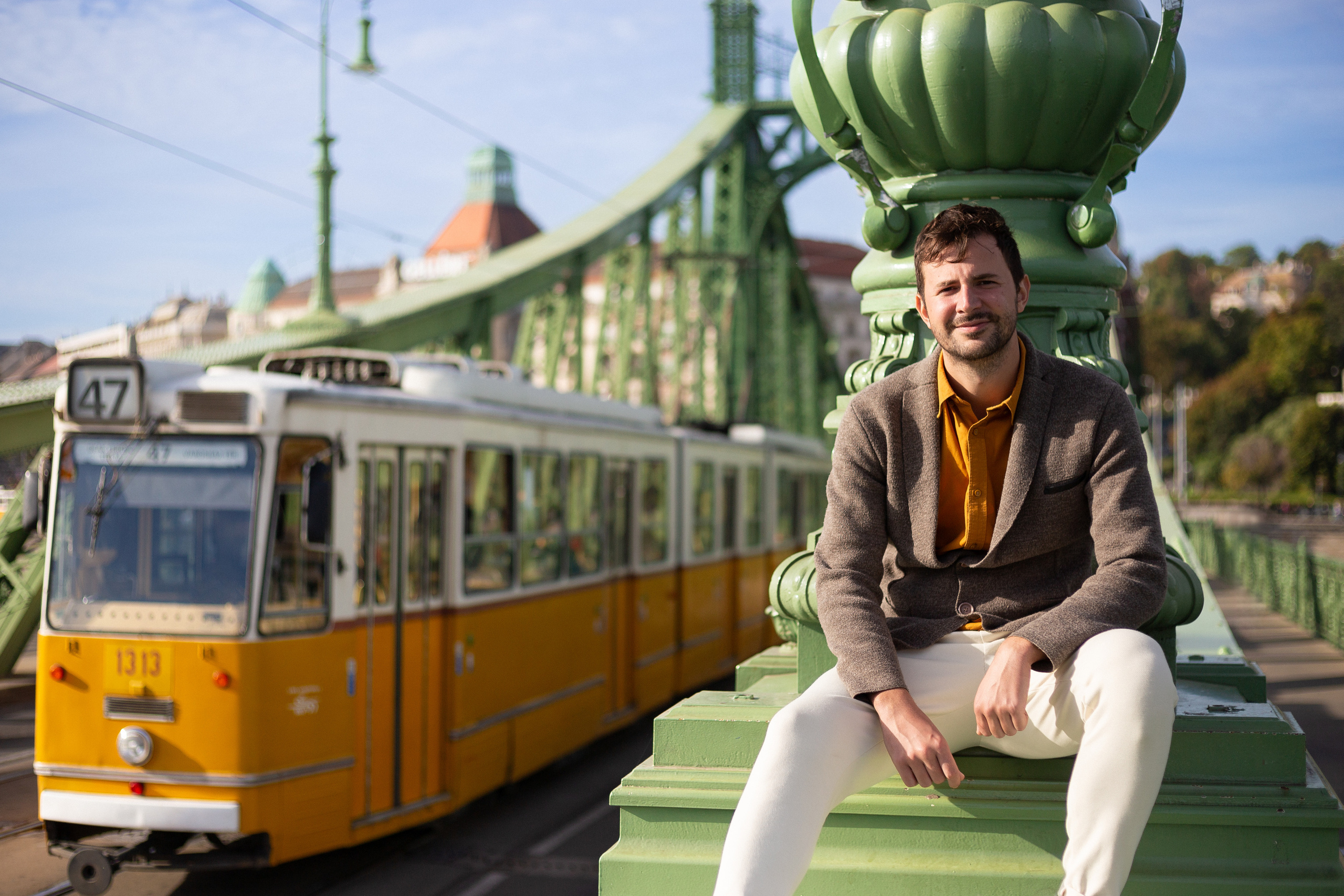a man is sitting in front of a yellow Budapest tram