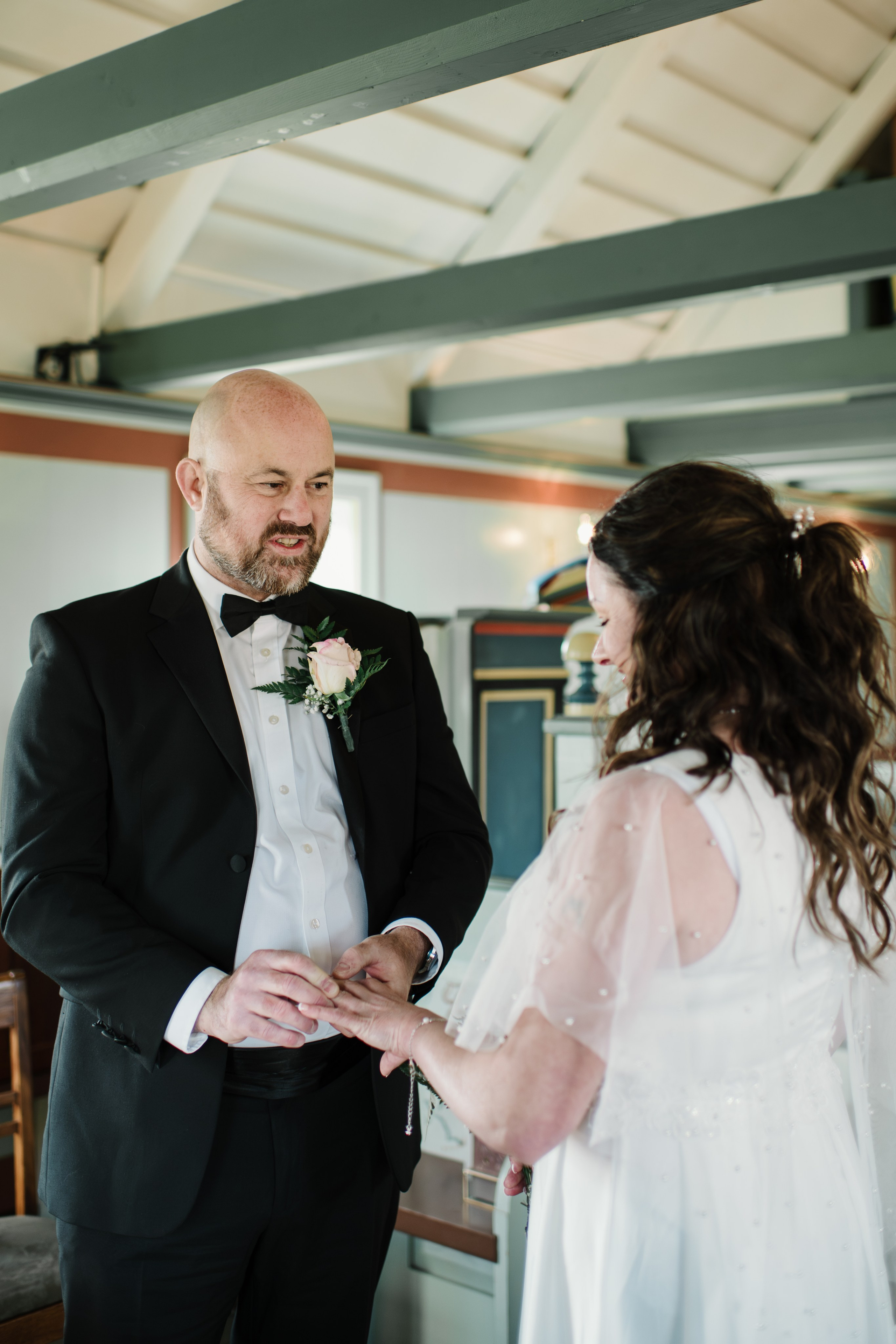 Intimate embrace between the bride and groom near the black church of Búðir, framed by rolling hills and an overcast sky.