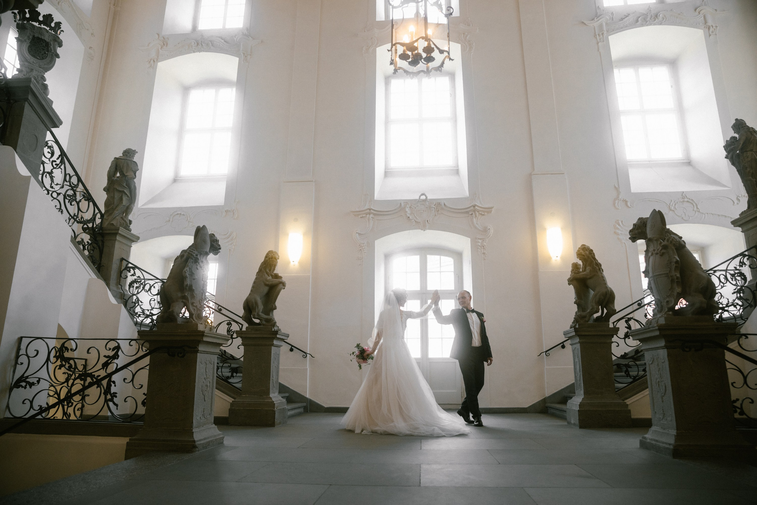 Bride and groom dancing by baroque staircase at Schloss Meersburg with statues nearby