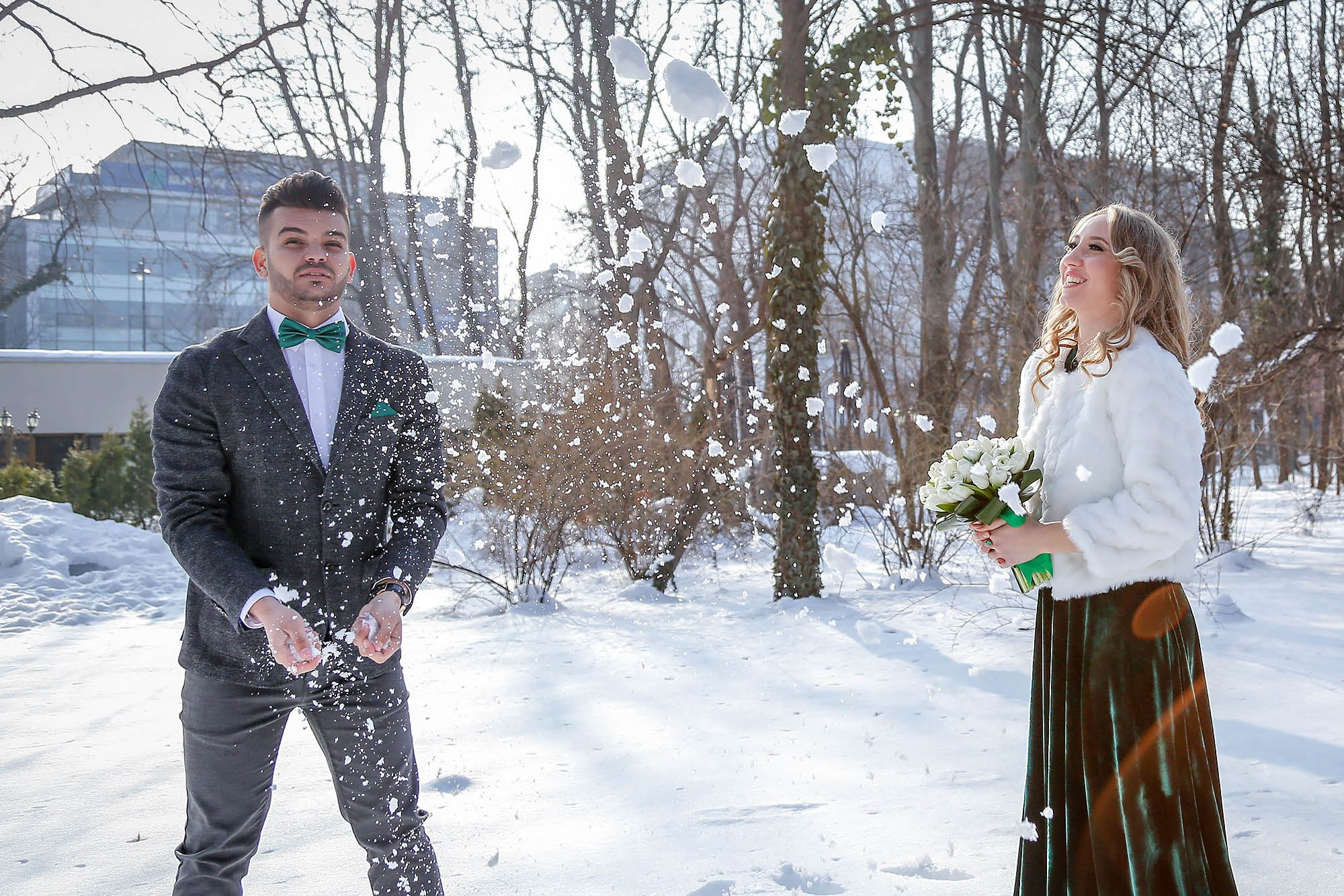 Happy and playful newlyweds throwing snow into the air, a fun and dynamic moment during their winter photo shoot.