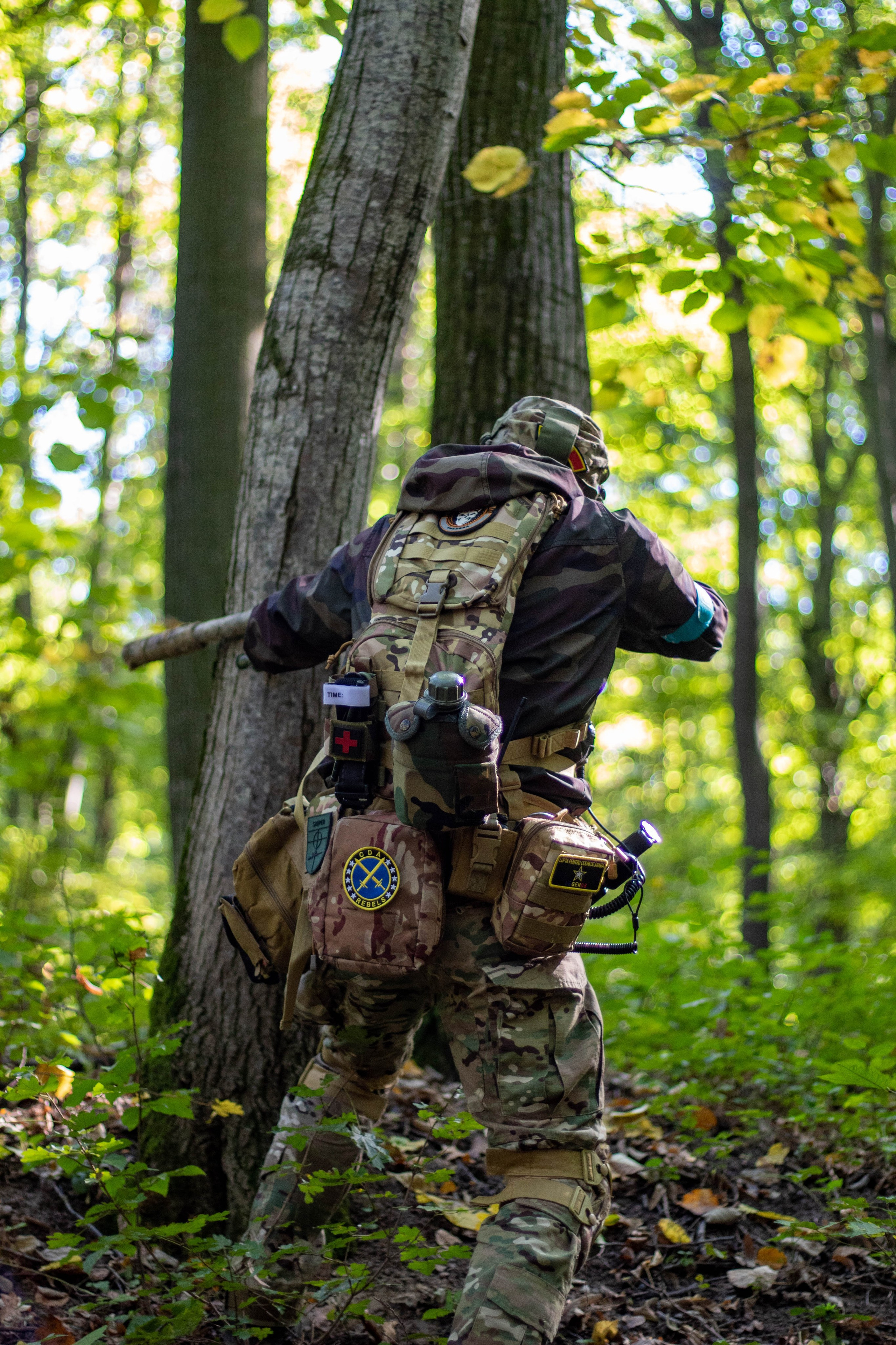 Airsoft player in a ghillie suit walking through the woods during a match.