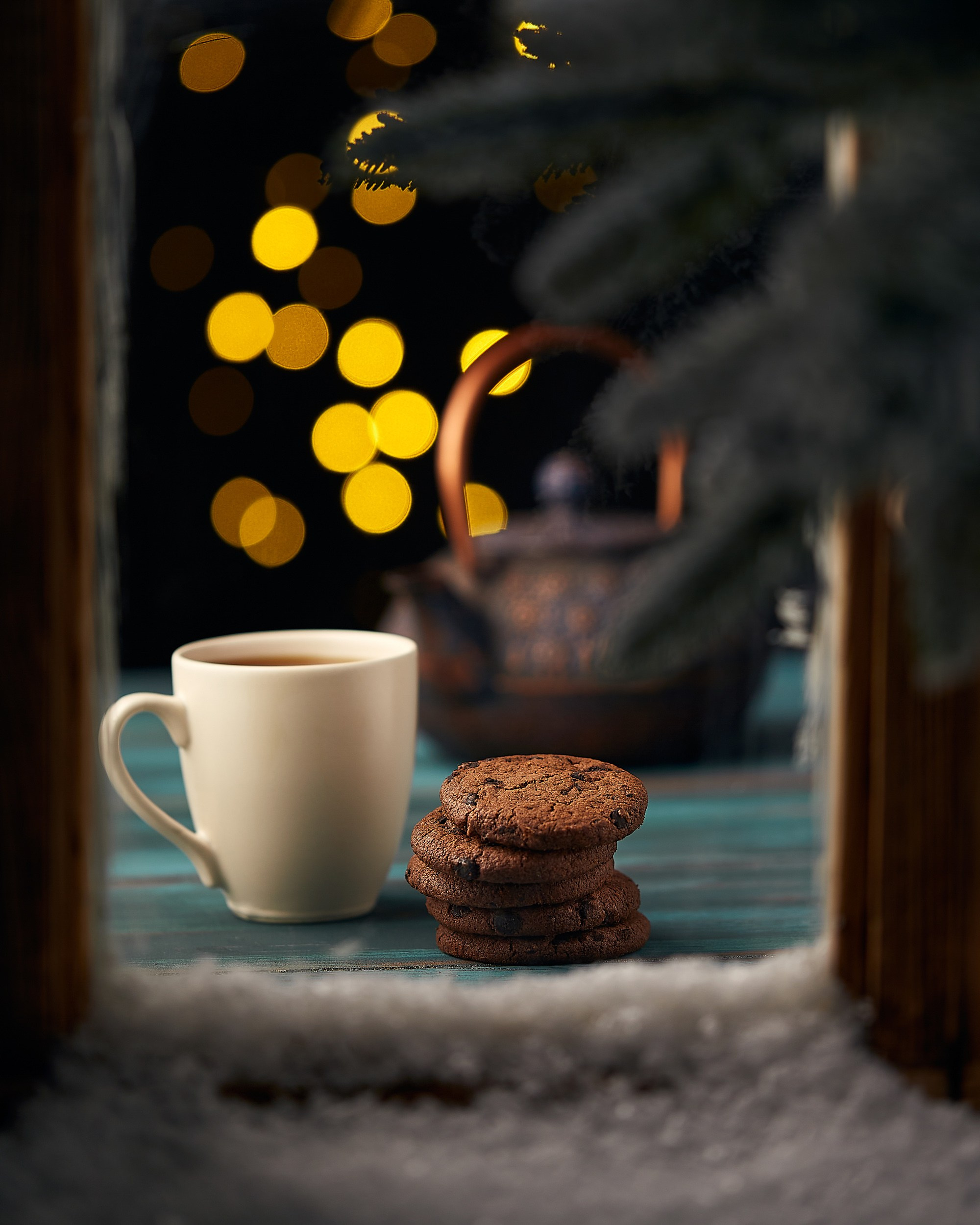 Qış dekorunda şokoladlı peçenye və isti çay fincanı, fonunda işıqlar