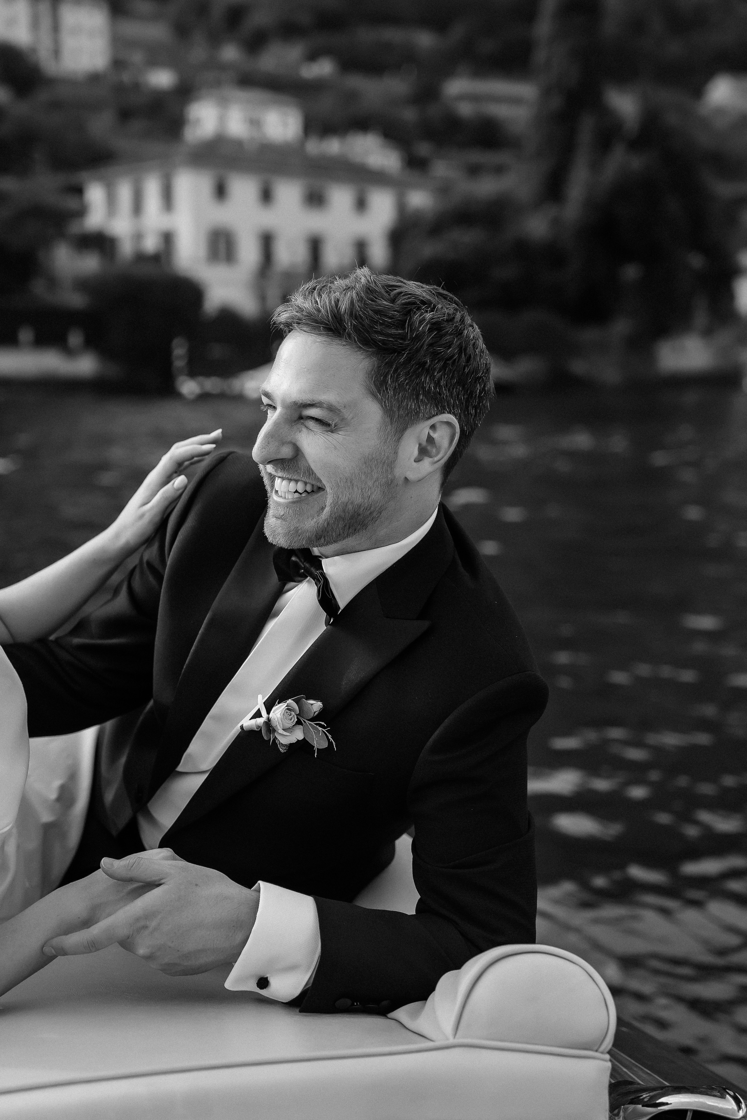 Black and white photo of the groom laughing on the boat at Villa Lario, Lake Como, Italy