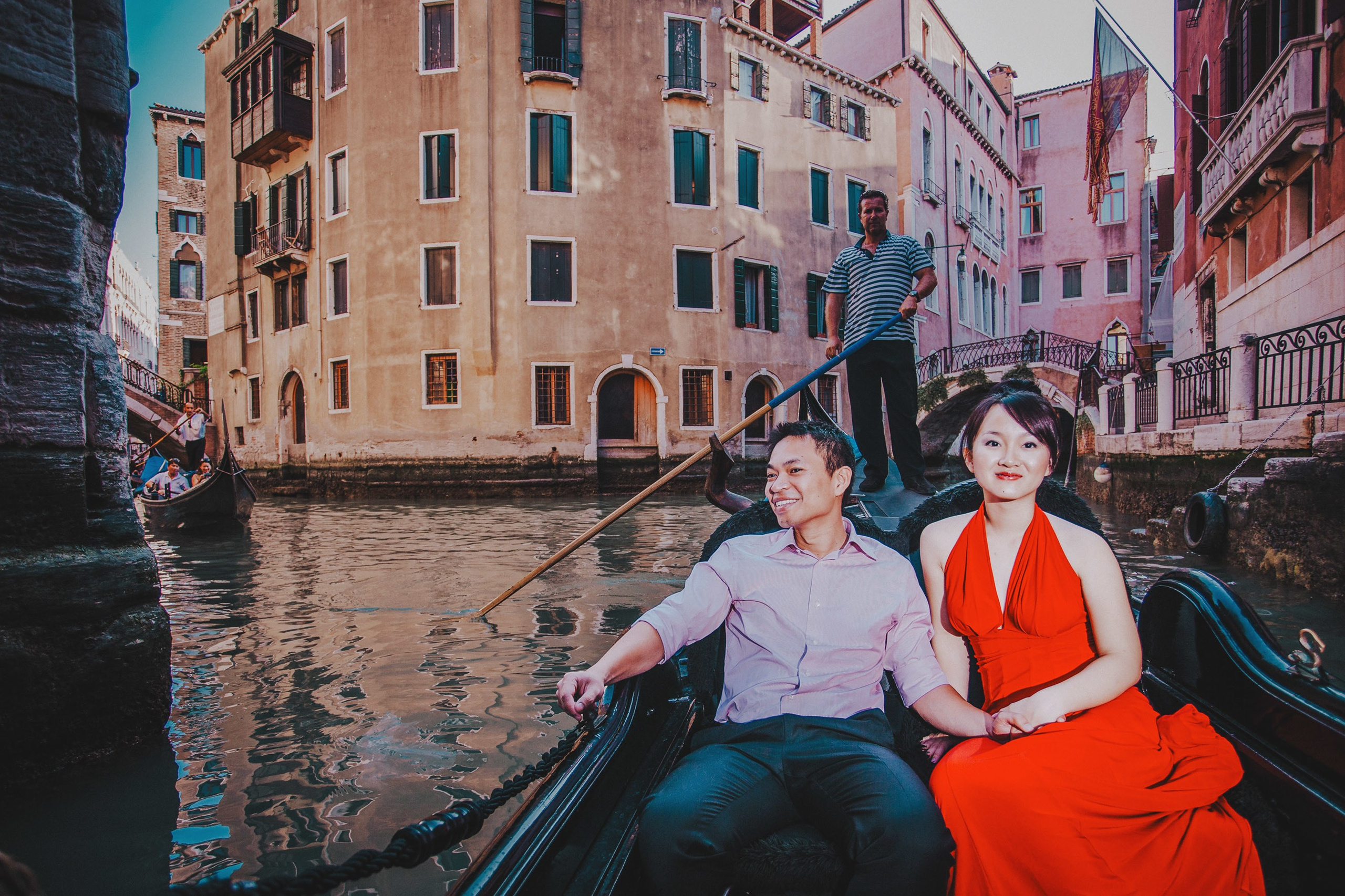 Smiling Thai couple holding hands exploring Venice aboard gondola.