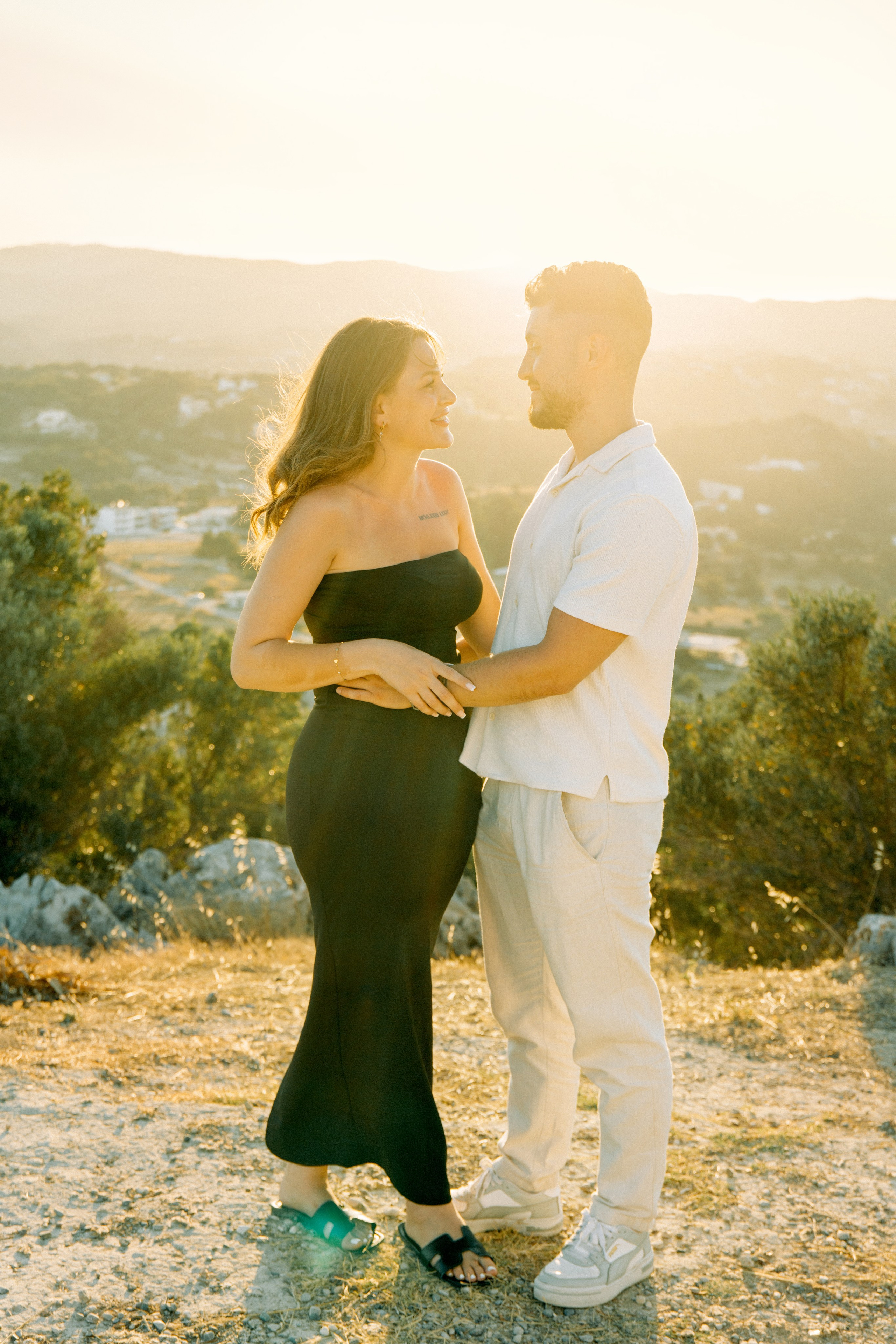 "Liebevoller Blickkontakt: Ein Paar auf dem Felsplateau des Profitis Ilias vor der Kulisse von Faliraki und dem Mittelmeer."