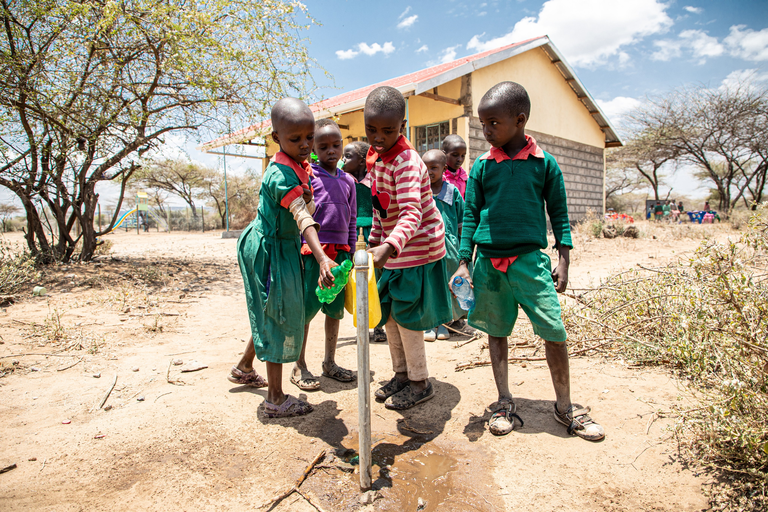 A close-up wide angle photo of children scrambling at a tap water point in Oloomaiyana in Kajiado county. Documentary photography
