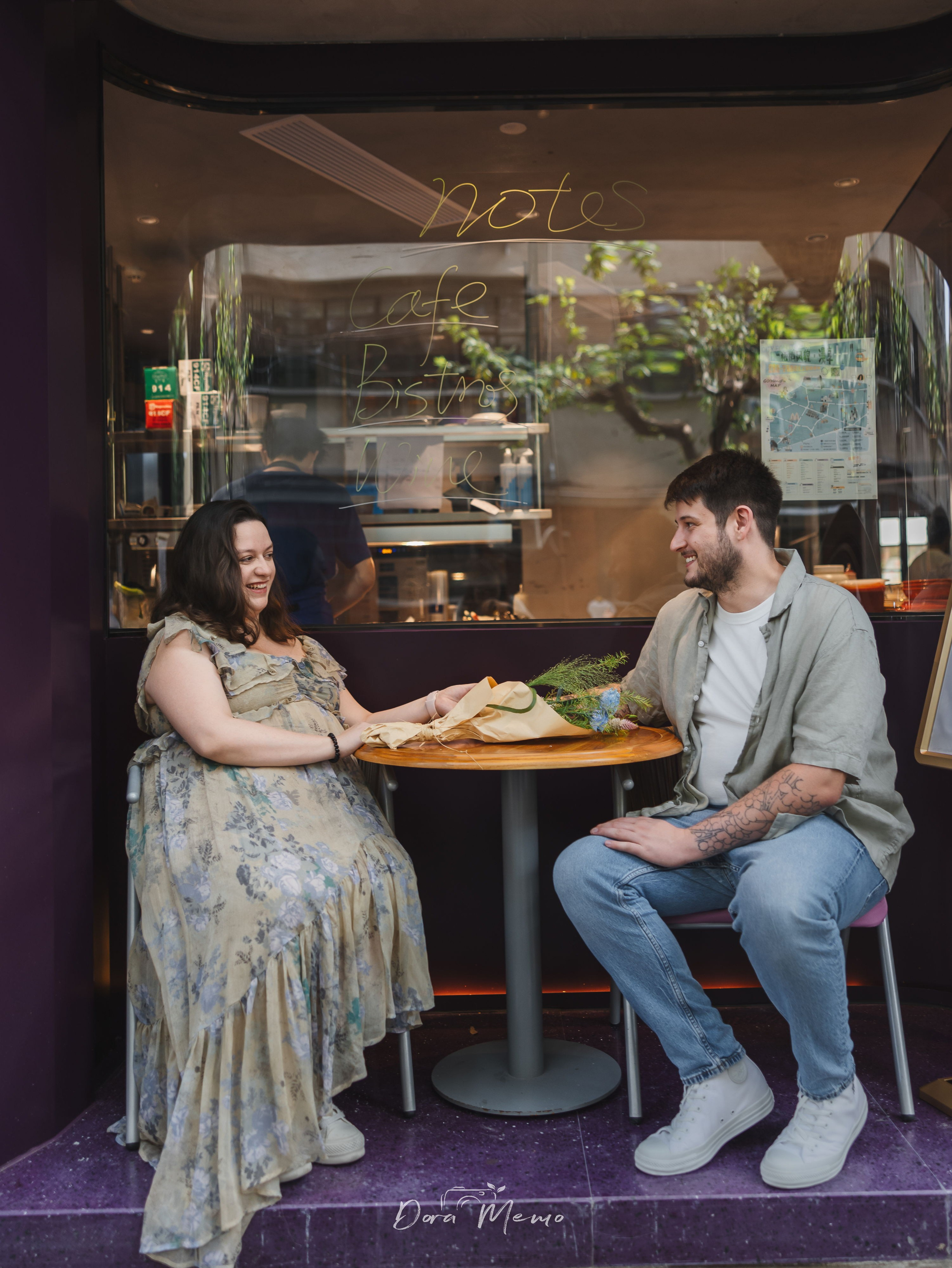 A relaxed couple sitting outside a cafe, smiling at each other during their maternity photoshoot in Shanghai.